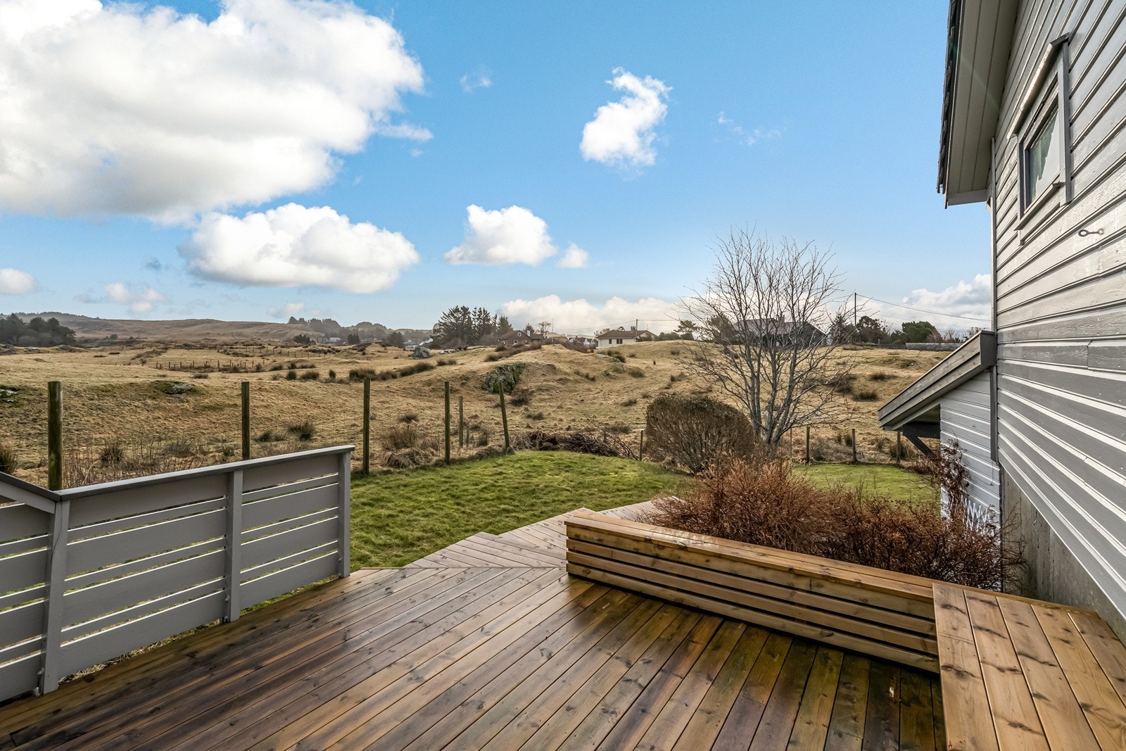 Terrasseplatting i tre med fastmonterte benker og plen på siden. Galleribilde