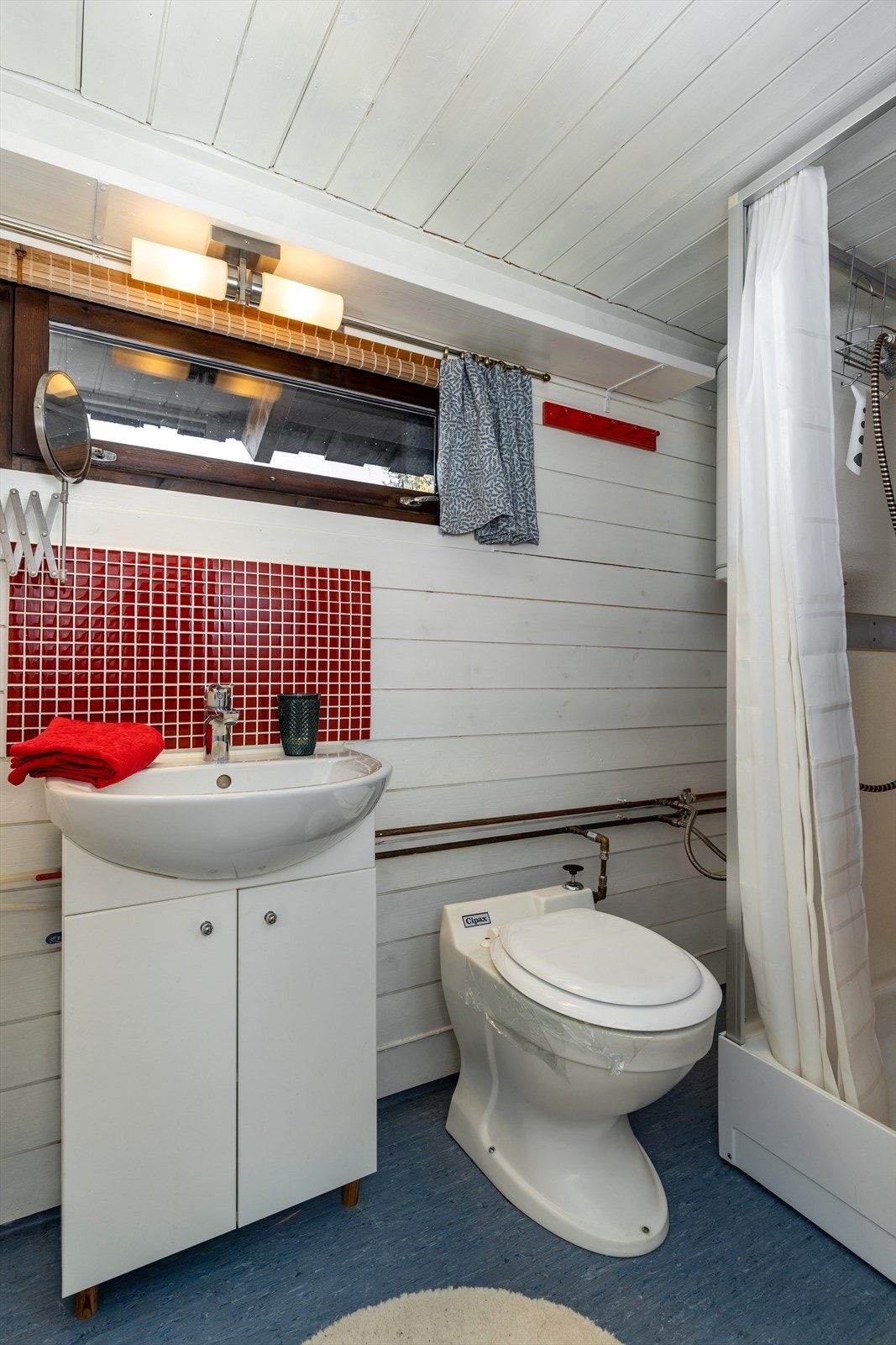 Badet har servantinnredning, håndvask, eldre type av vakumtoalett, dusjkabinett med forheng. Galleribilde