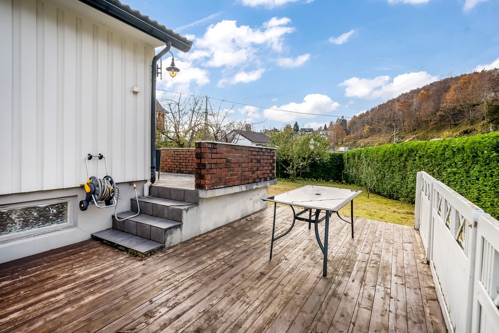 Flat tomt med terrasse, plenlagte områder, hekk og noe beplantning. Galleribilde