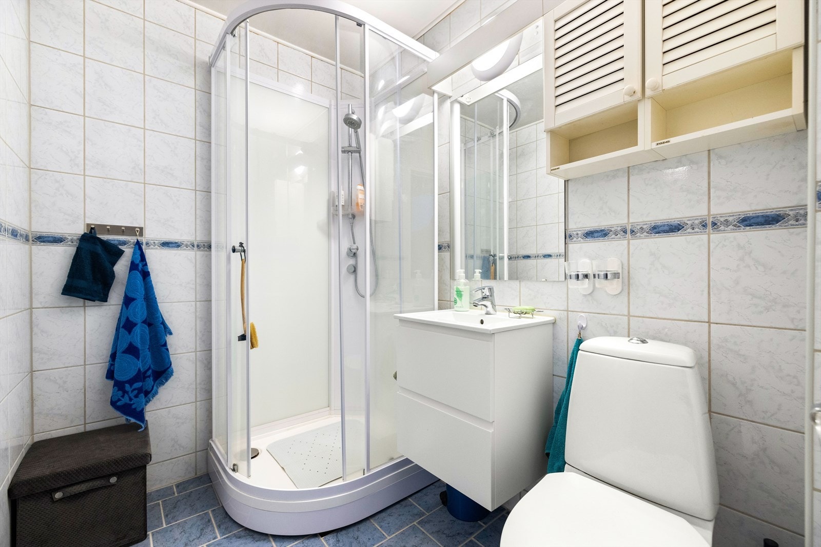 Pent flislagt baderom bestående av klosett, servant nedfelt i innredning, speil og dusjkabinett. Galleribilde