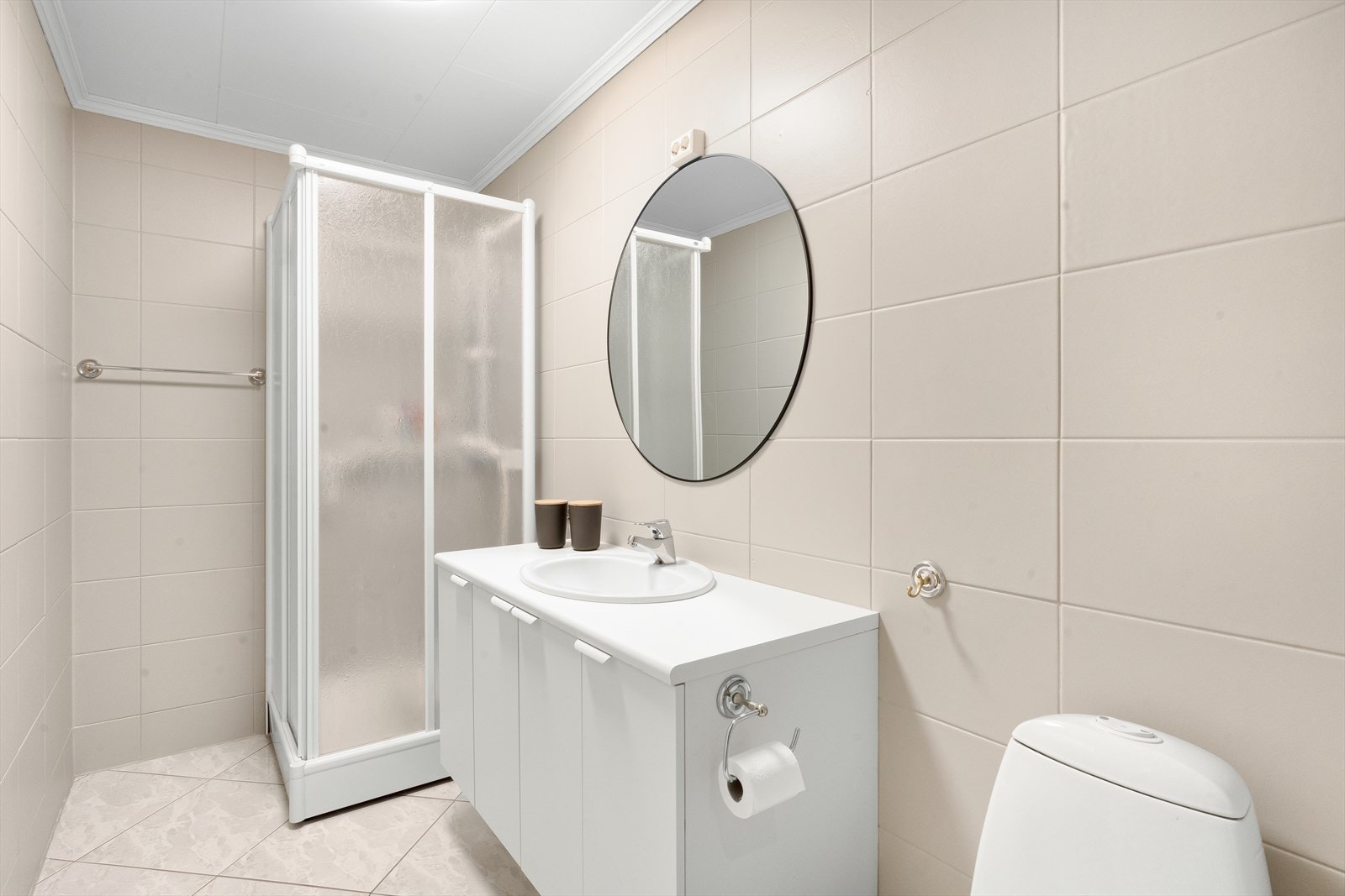 Pent helfliset bad med varme i gulv, malt himling. Lys, pen baderomsinnredning med nedfelt servant, moderne rundt overspeil. Dusjkabinett og wc. Galleribilde