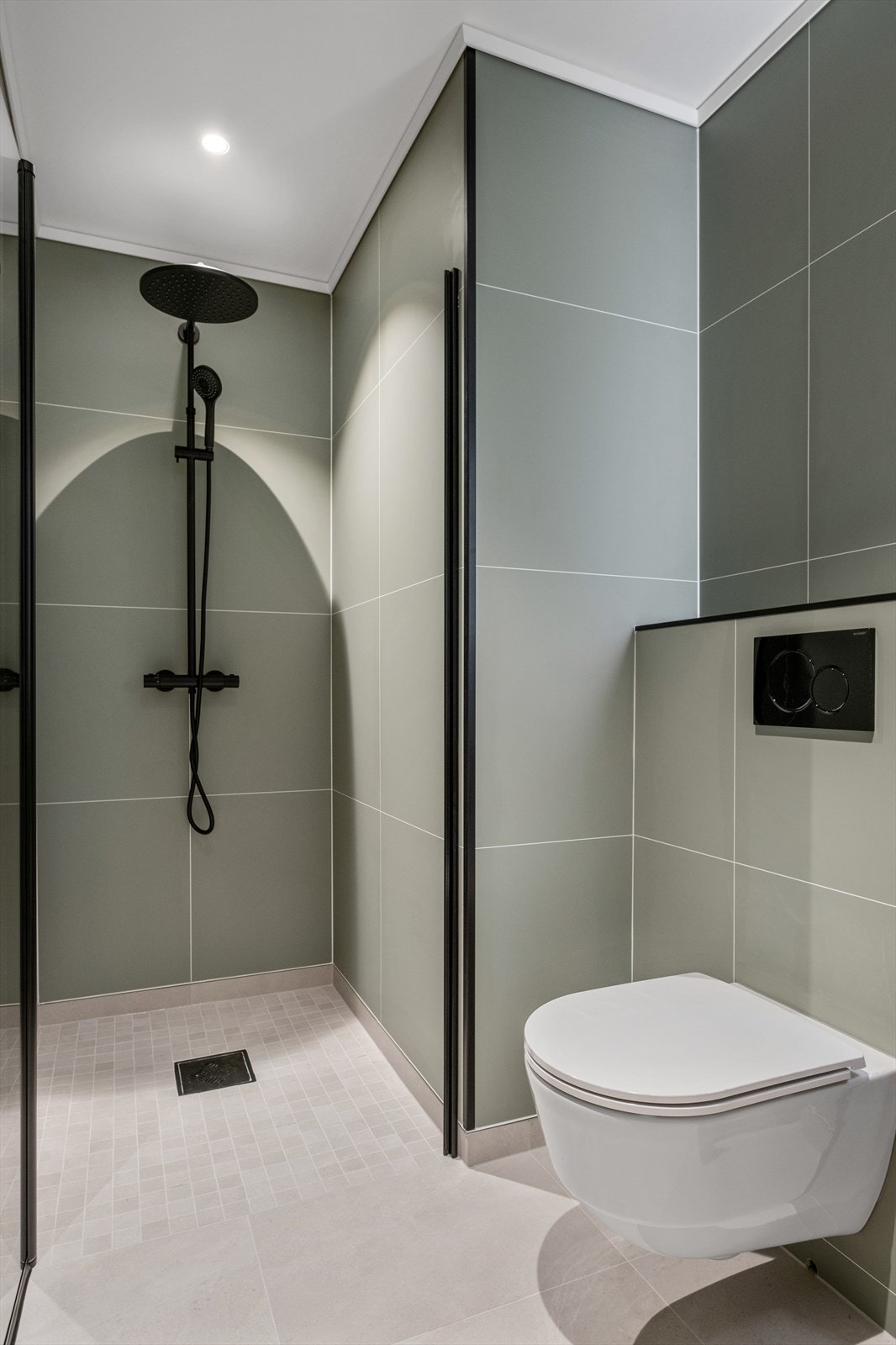 Badet inneholder vegghengt toalett, dusj, servantinnredning og speil med lys. Galleribilde