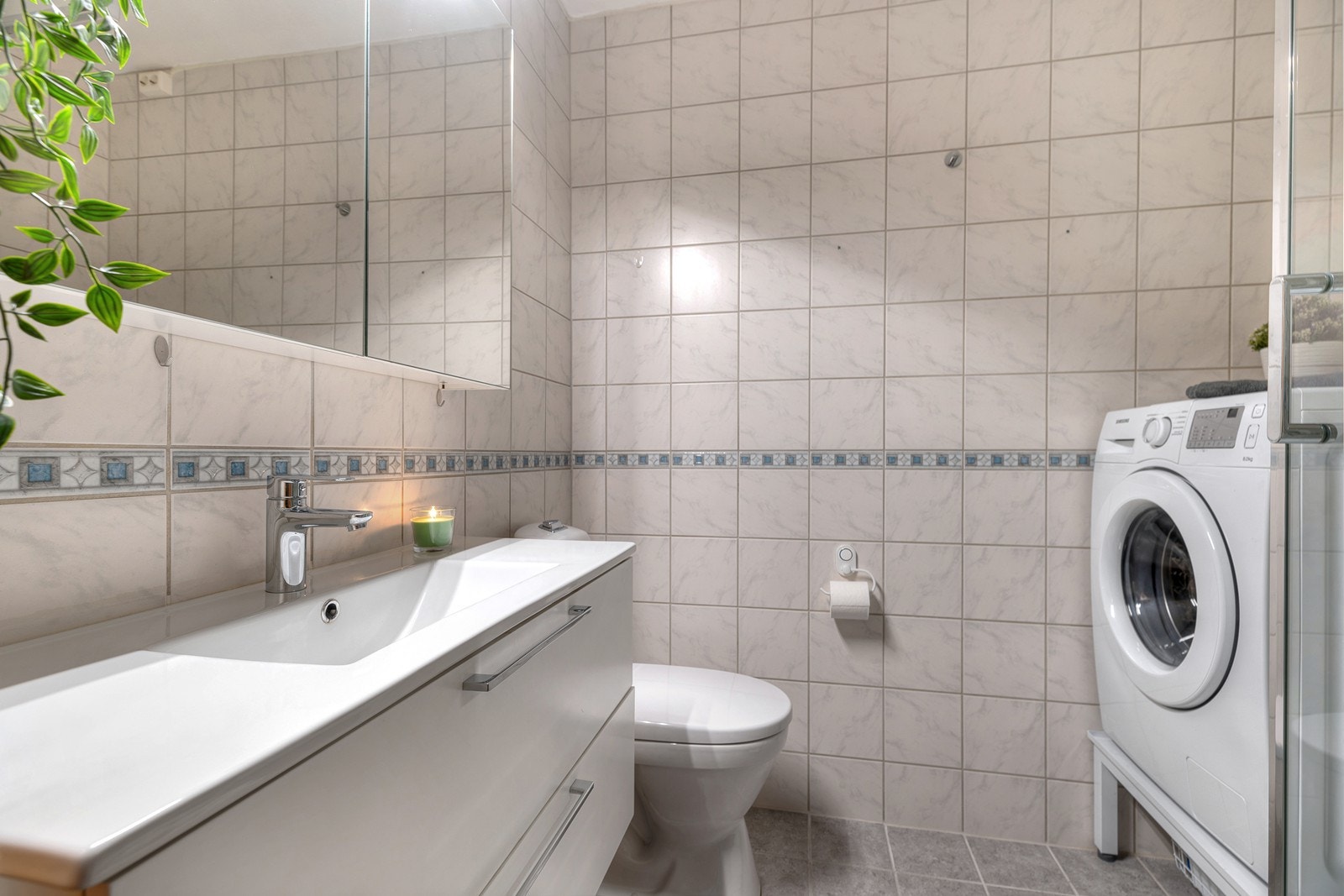 Flislagt bad med dusjkabinett, toalett, servant, overskap med speil og opplegg til vaskemaskin Galleribilde