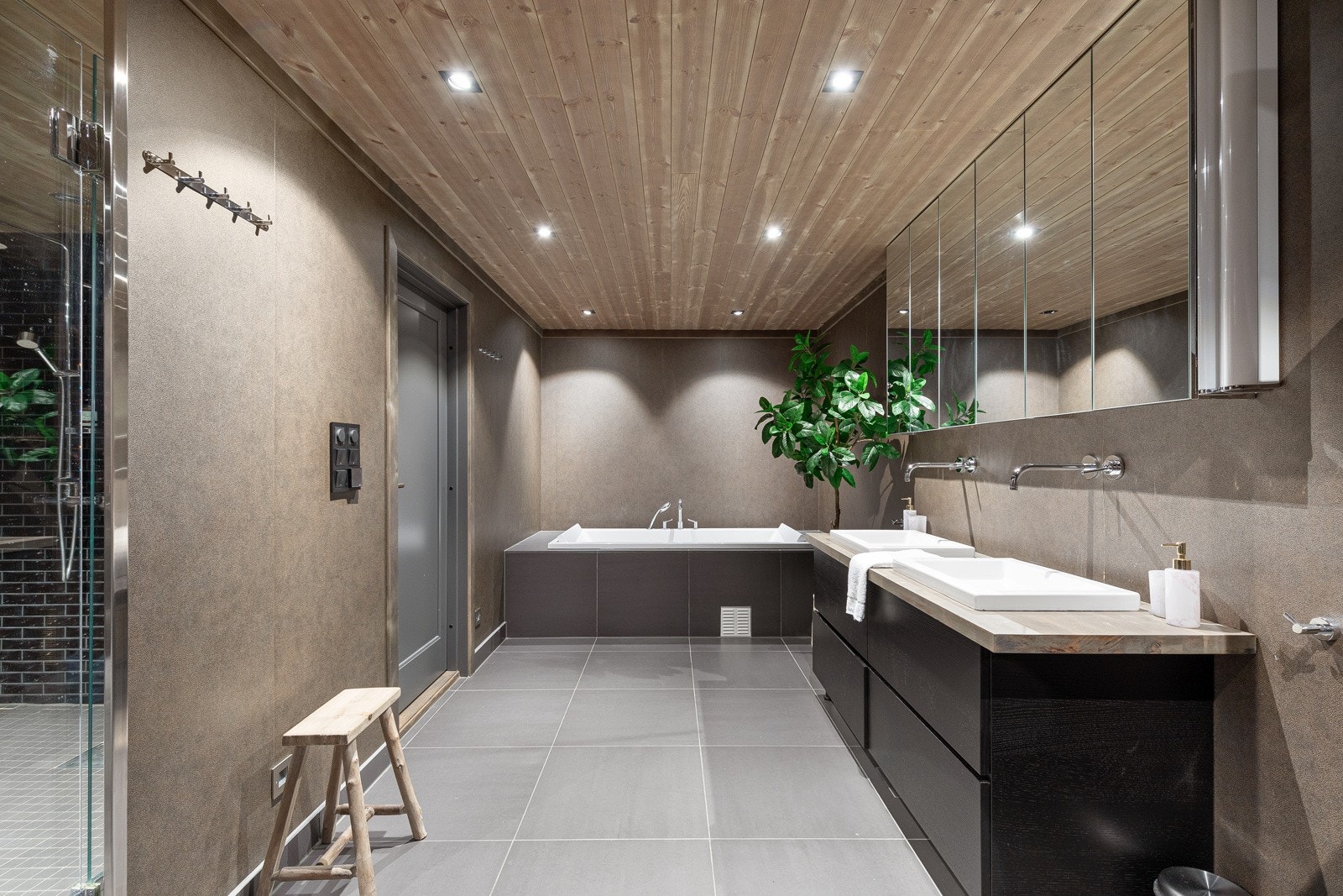 Innflisa badekar, vegghengt wc, stor innreiing med skuffer, benkeplate med 2 nedfelte servantar og tilhøyrande speigelskap med lys. Galleribilde