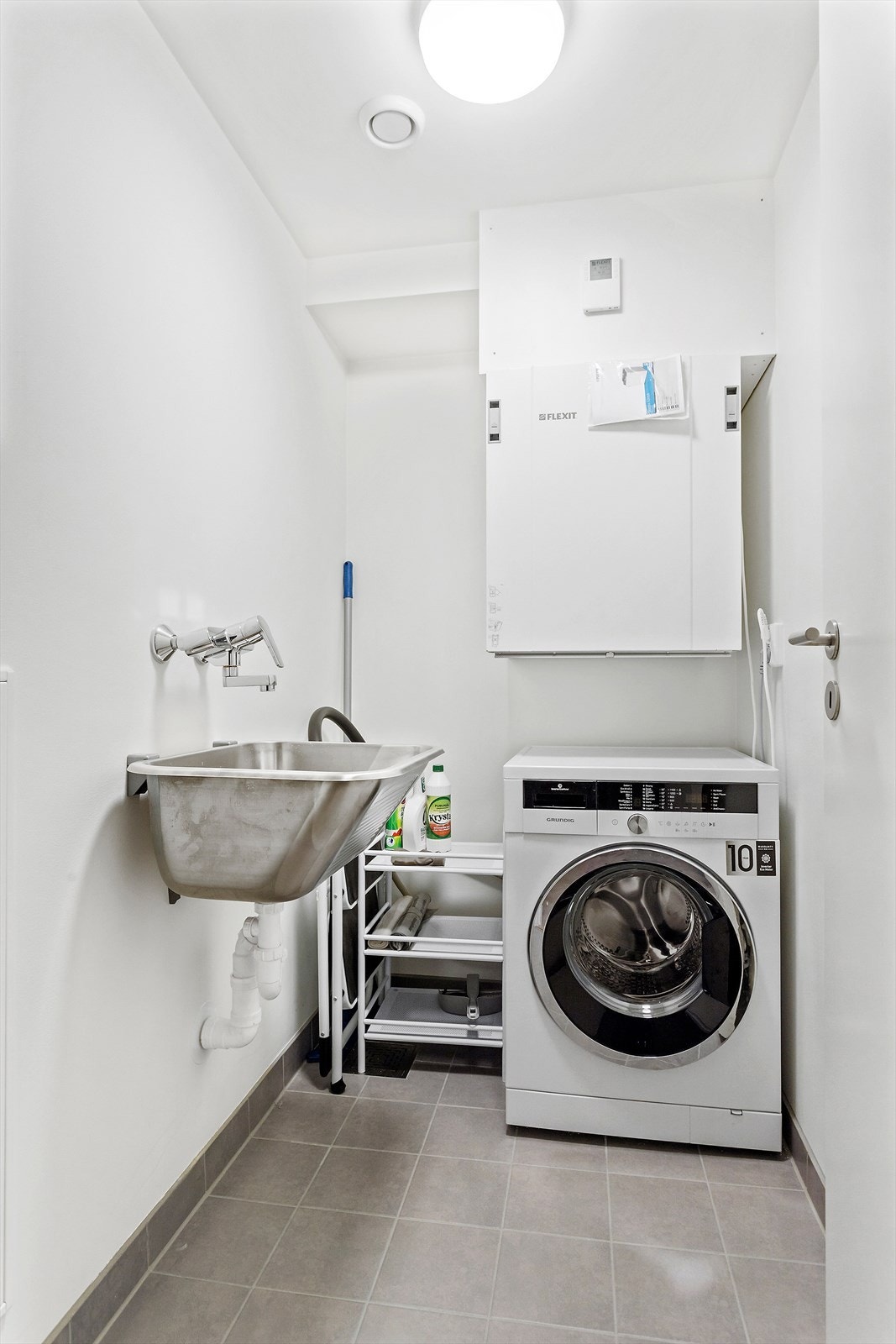 - Vegg i vegg med badet er et separat vaskerom/teknisk rom med flislagt gulv og vannbåren gulvvarme. Vaskerommet er praktisk utstyrt med veggmontert utslagsvask av stål - i tillegg til opplegg for vaskemaskin - Galleribilde
