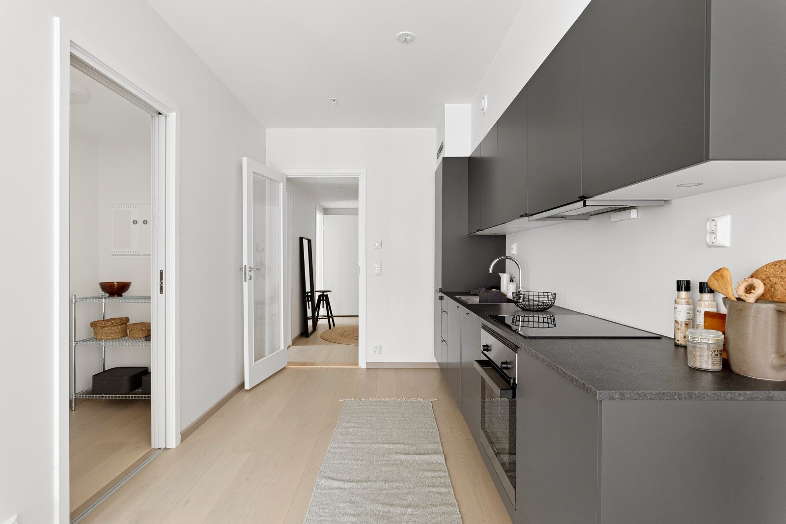 Innredningen har grå glatte fronter og mørk grå laminert benkeplate med nedfelt oppvaskkum. Praktisk med spotter innfelt under overskap. Galleribilde