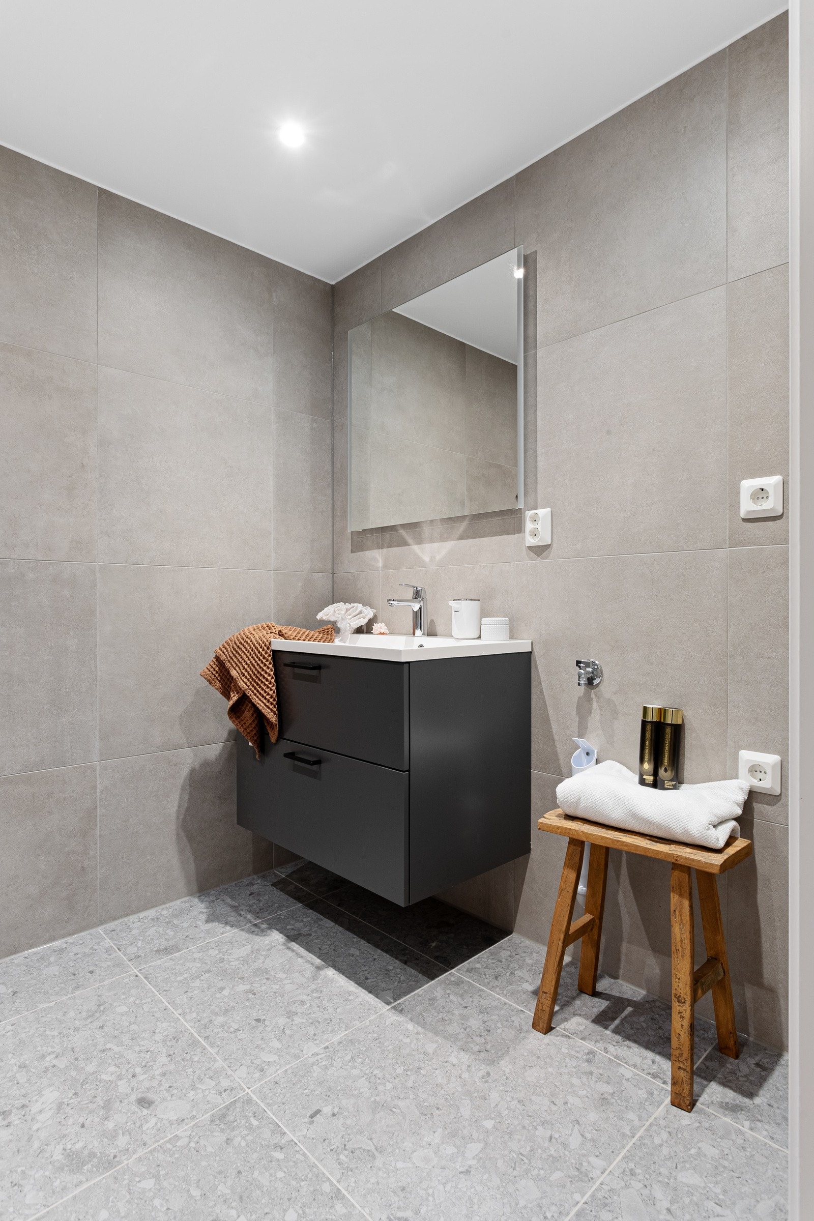 Baderommet har delikate 60x60 fliser på gulv og vegger, deilig gulvvarme og downlights i himlingen. Flisene har fint spill i seg som tilfører liv til det grå og passer godt sammen med armatur og detaljer i krom. Galleribilde