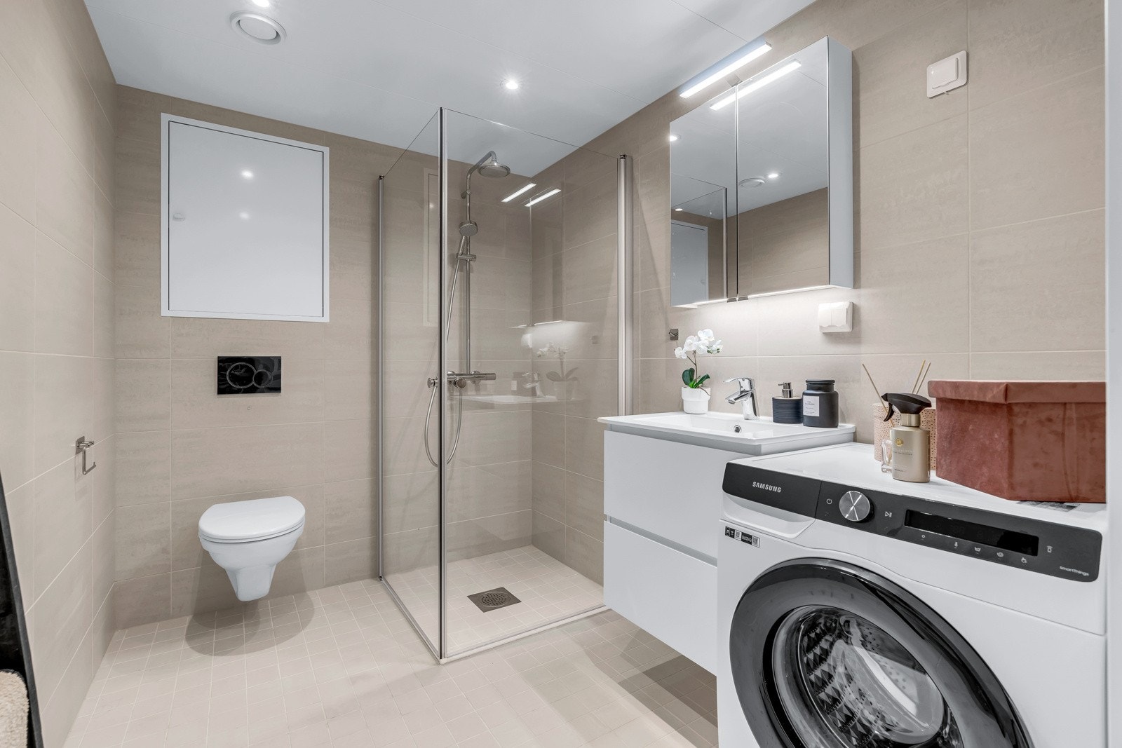 Stort bad med dusjsone, vegghengt toalett, servant med speil med belysning og god plass til vaskemaskin og tørketrommel Galleribilde