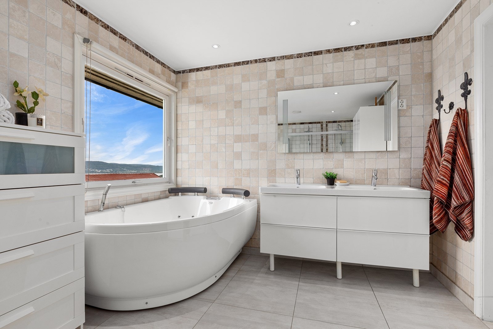 Badet er av god størrelse og inneholder dobbel servant med underskap, speilskap med lys, toalett, badekar og romslig dusjnisje med fast skyvefelt og dobbel regndusj Galleribilde