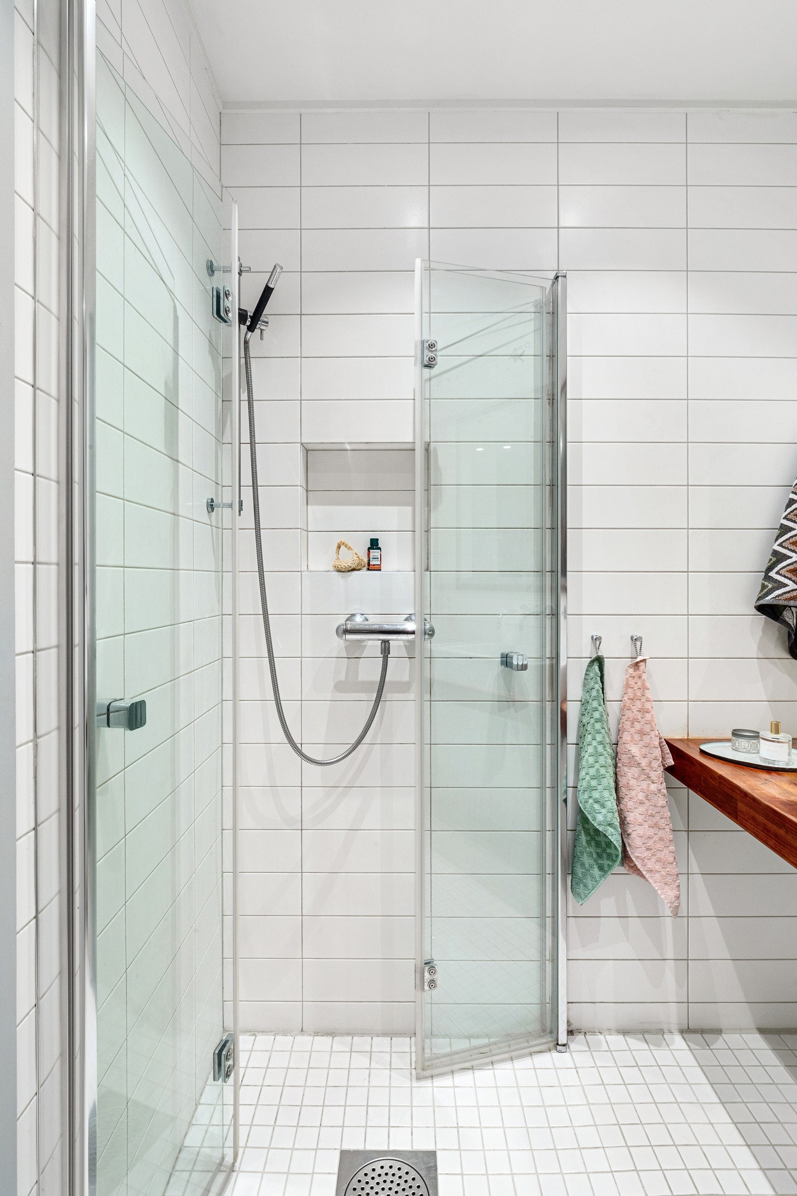 Badet innholder ovenpåliggende servant med ett-greps armatur, innfelt speilskap, vegghengt toalett, dusj med innfellbare dører av glass og metall. Galleribilde