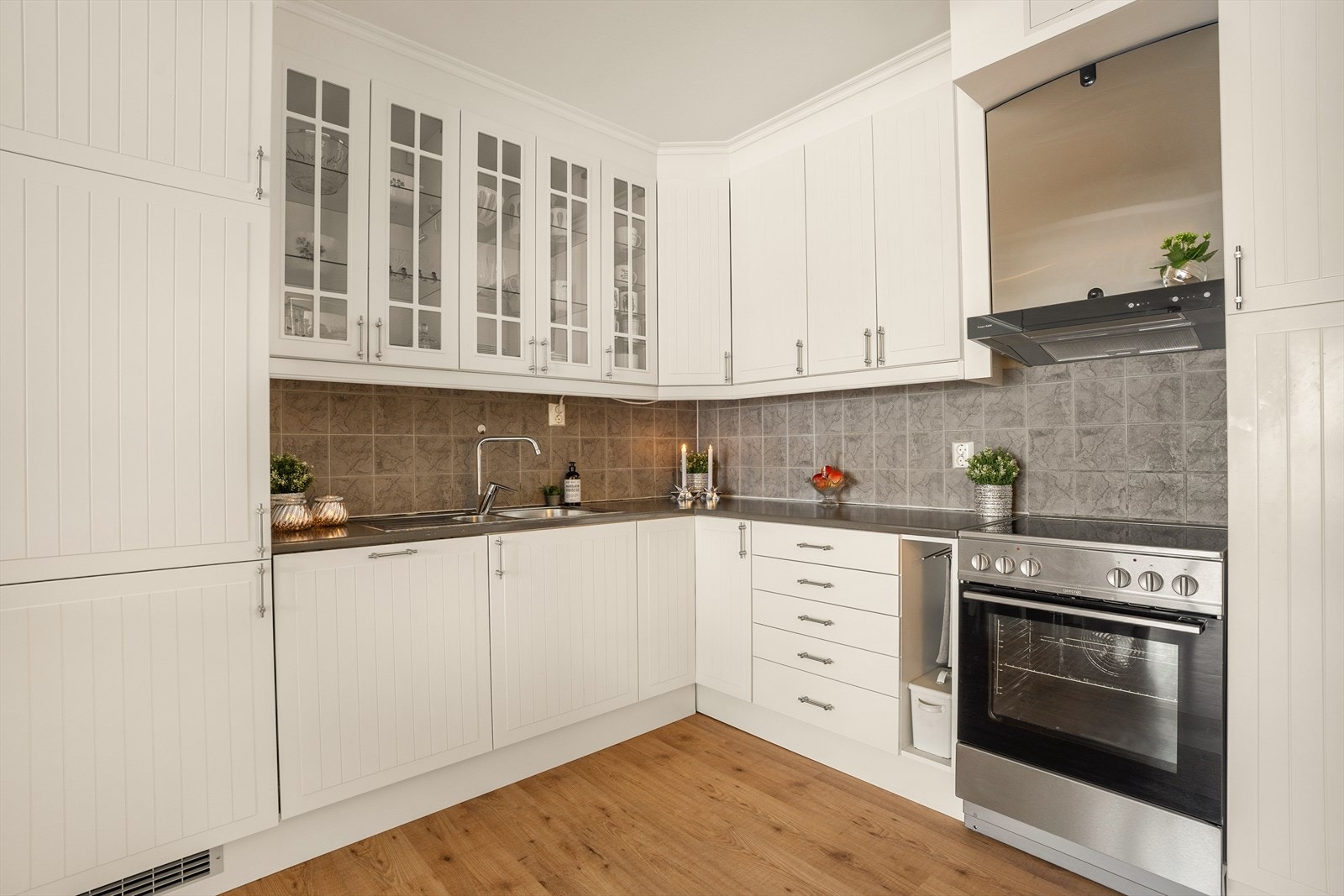 Kjøkkeninnredning med profilerte fronter, to overskap har glassfronter, heltre benkeplate, over benkeplaten er det
benyttet fliser, stål oppvaskkum, ventilator. Galleribilde