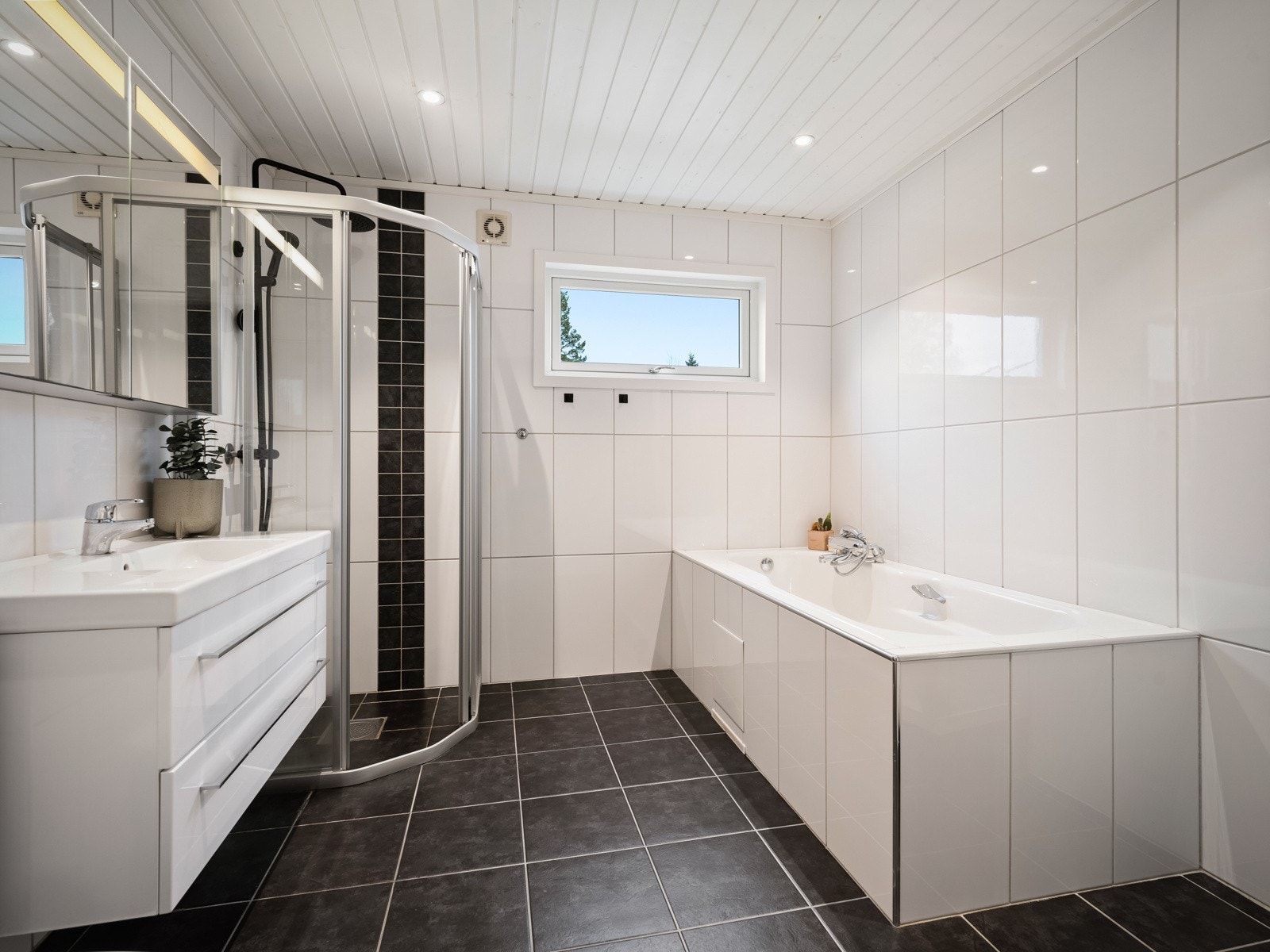 Hovedbadet har fliser på gulv og vegger, vegghengt klosett, badekar og dusjnisje. Galleribilde