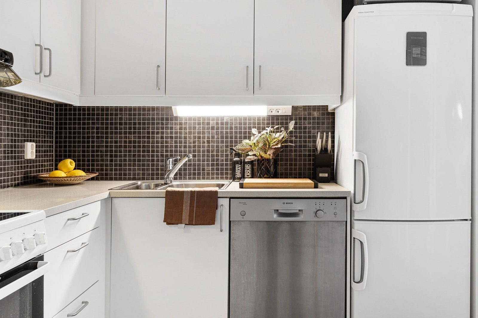 Det er fliser på vegg mellom kjøkkenbenk og overskap. Benkeskapsbelysning og stikkontakter er montert under overskap. Galleribilde