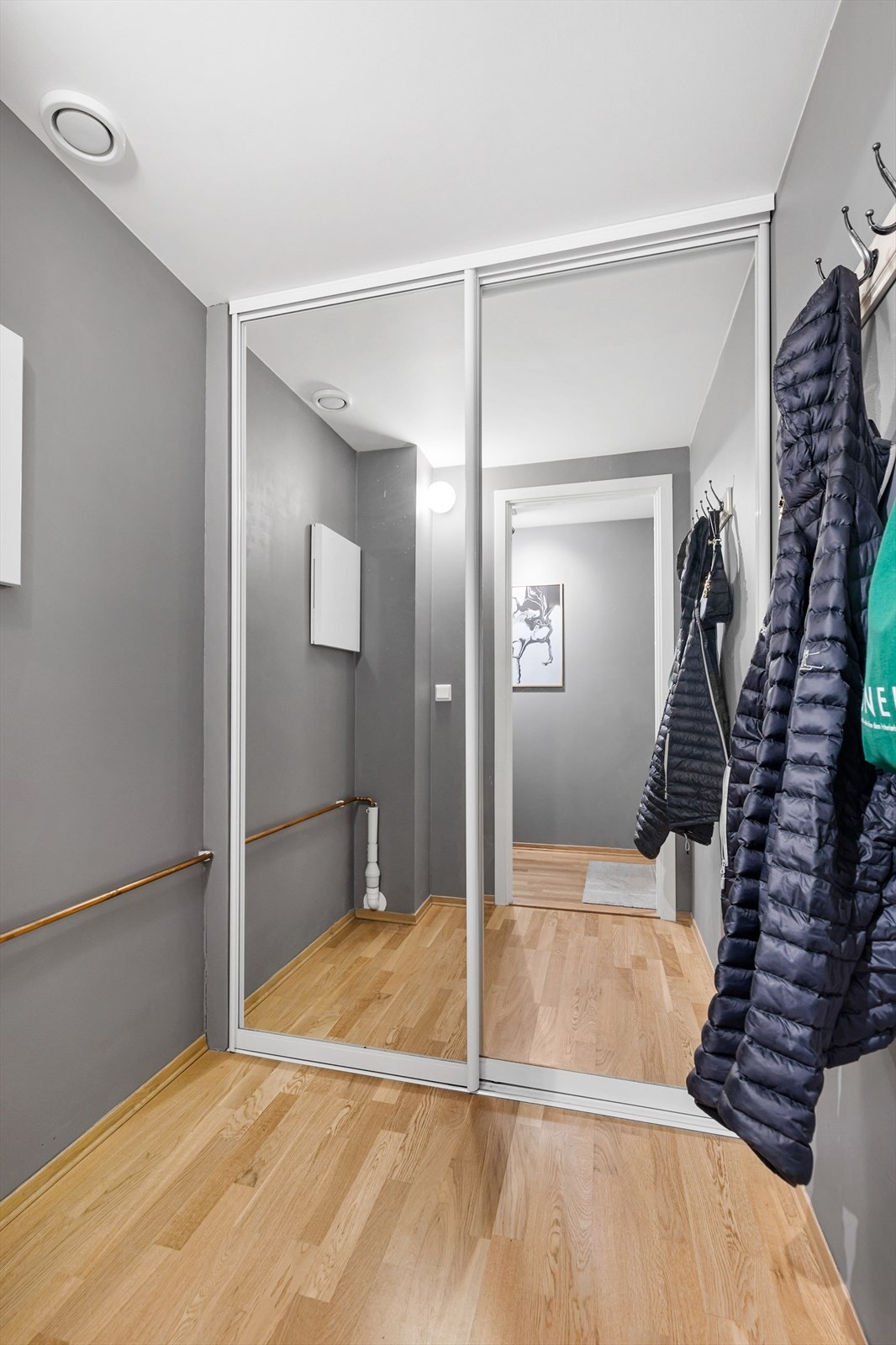 Innerst i rommet er det skyvedørsgarderobe med speilfronter. I tillegg er det mulighet for oppheng av jakker på vegg, samt plass til en benk eller skohylle. Galleribilde