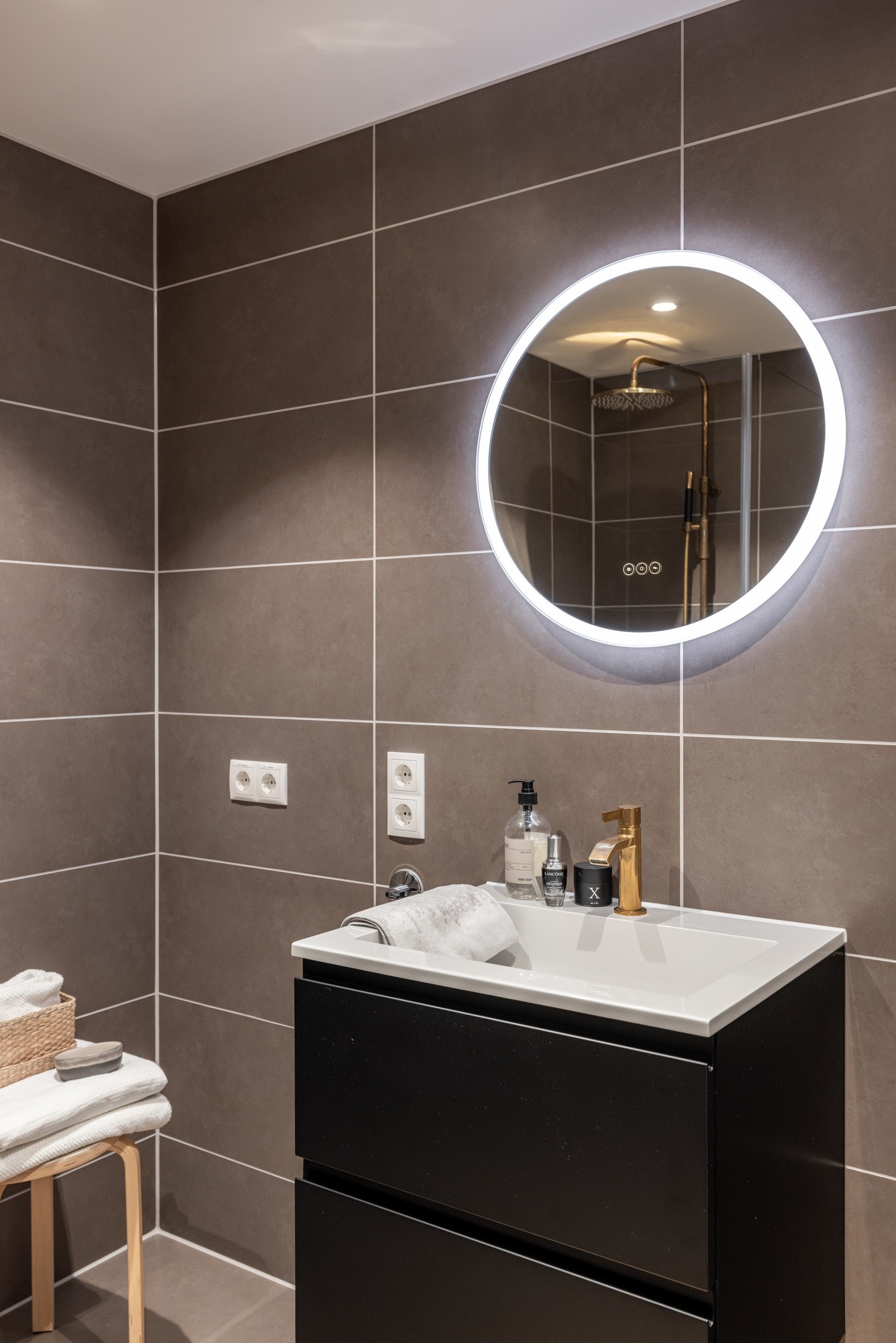 Moderne baderomsinnredning med skuffer og heldekkende servant med armatur i messing, rundt speil med integrert belysning over. Gjennomgående detaljer i messing gir et lekkert uttrykk som har det lille ekstra for å gi deg glamourfølelsen i hverdagen. Galleribilde