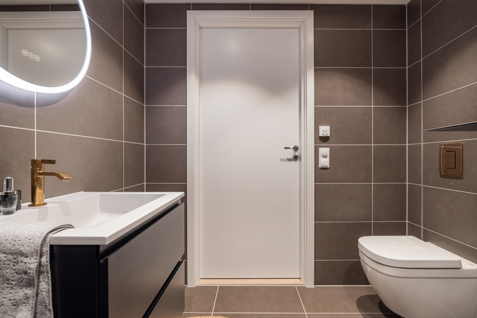 Baderommet er også utstyrt med nedsenket dusjhjørne med glassdører og både hånd- og regnfallsdusj i messing, samt vegghengt toalett. Plass og opplegg for vaskemaskin og tørketrommel over om ønskelig. Galleribilde