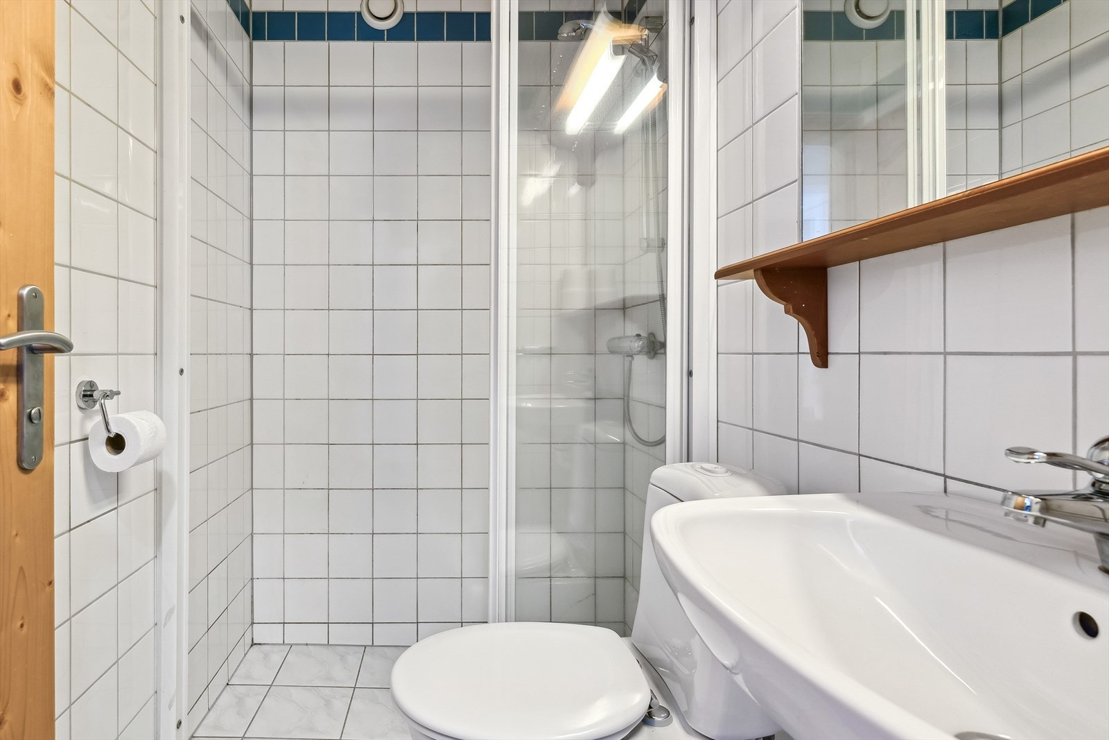 Badet er innredet med fliser på gulv, og vegg. Gulvmontert toalett, og dusj med dusjdører. Galleribilde