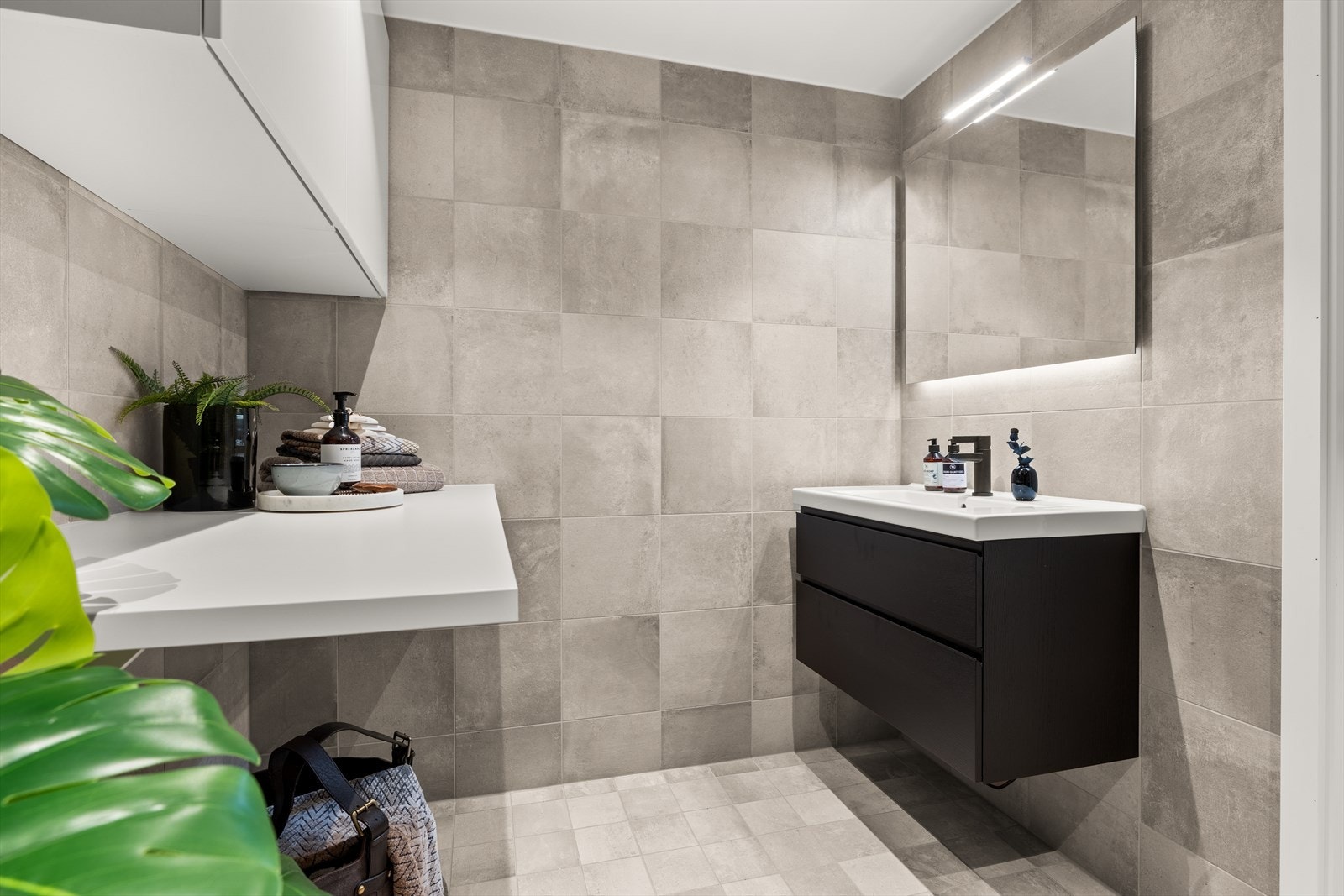 Badet er innredet med vegghengt klosett og servant med innredning. Det er opplegg og plass for både vaskemaskin og tørketrommel under den praktiske benken. Galleribilde