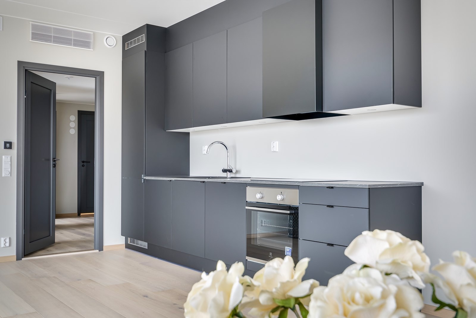 Delikat kjøkken i åpen løsning med stuen. Innredning med slette fronter i mørk, stilig utførelse. Galleribilde