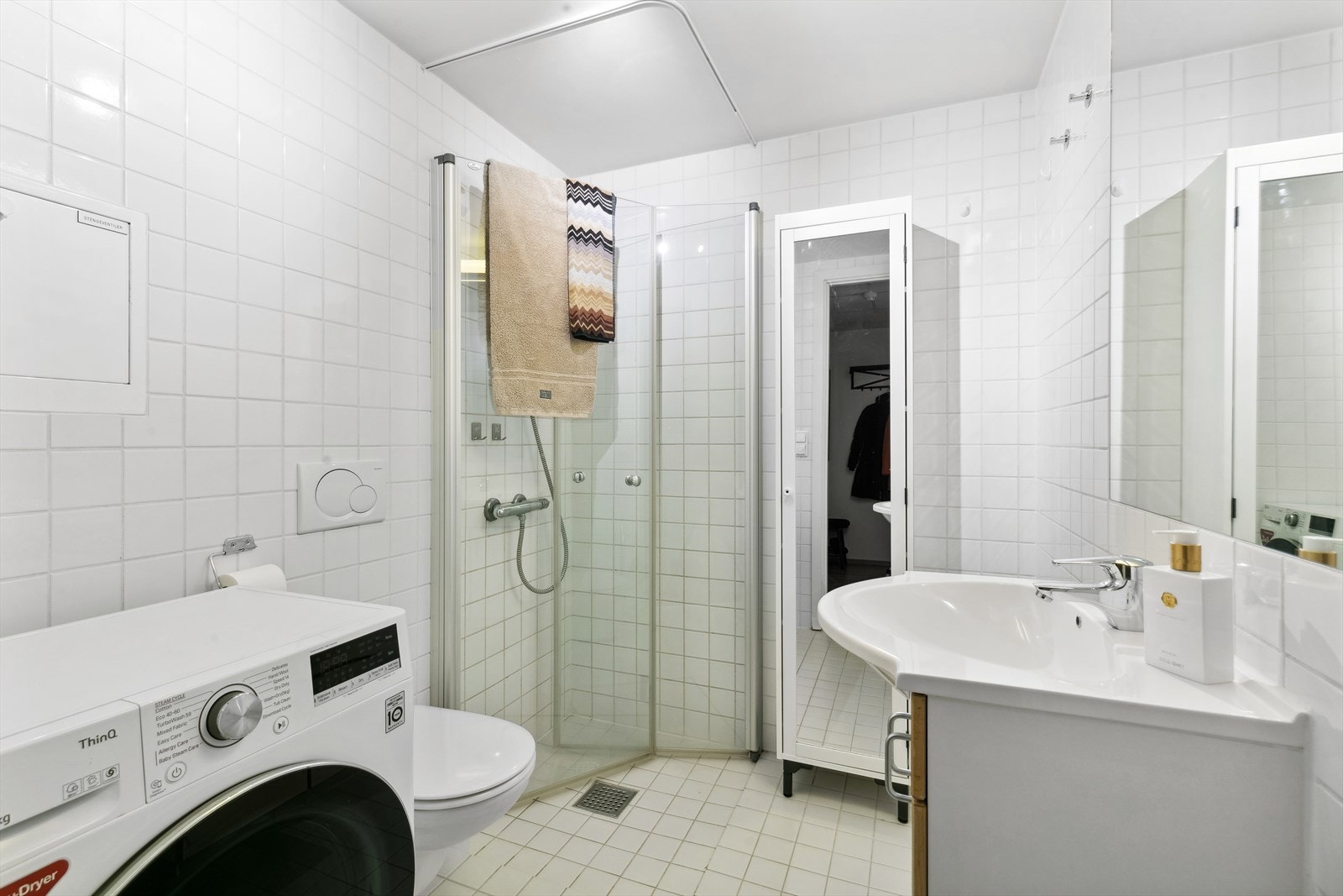 Baderom med vegghengt toalett og opplegg for vaskemaskin. Svingbare dusjdører i glass som gir god utnyttelse av badet. Galleribilde