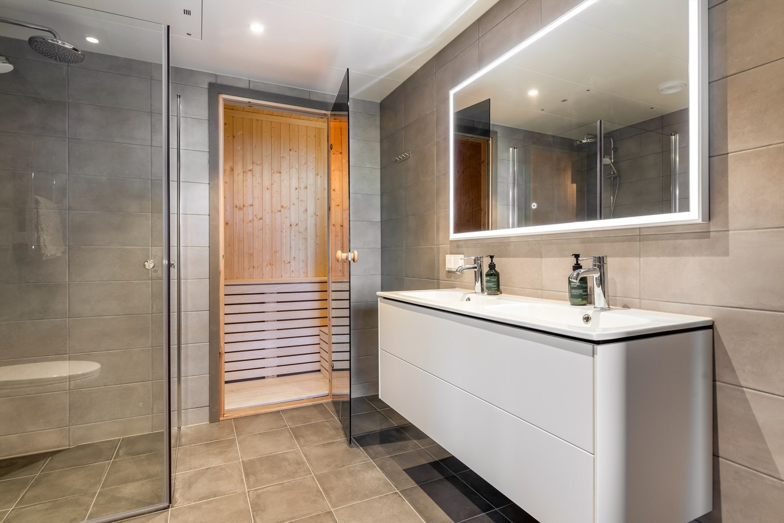 Badet har en romslig innredning med to heldekkende hvite vasker, underskuffer med slette fronter og speil med lys. Galleribilde