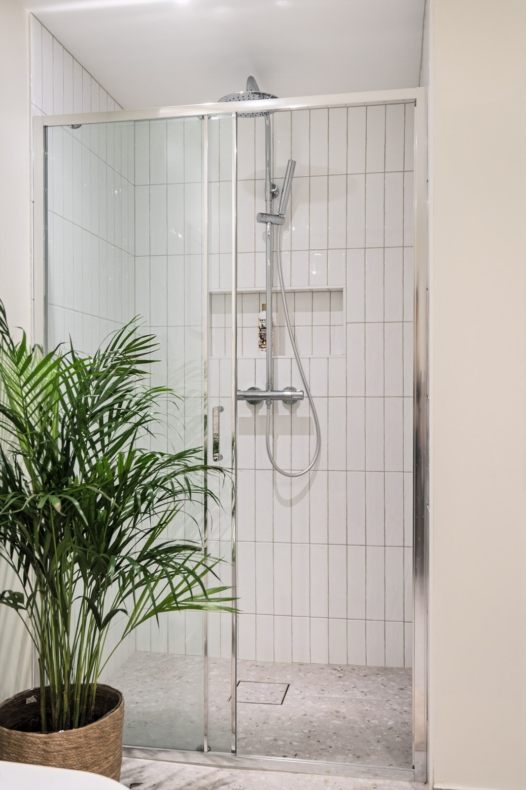 Stor dusj med glassdører og vegghengt dusjarmatur med regndusj. Legg merke til den innfelte og flislagte hyllen som er perfekt for oppbevaring av diverse såper og dusjprodukter. Galleribilde