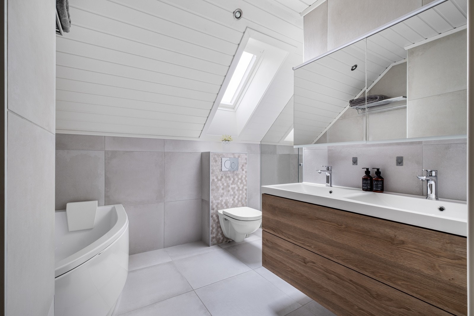 Badet har en praktisk vegghengt servantinnredning med skuffer og en dobbel ovenpåliggende servant med moderne armaturer. Galleribilde