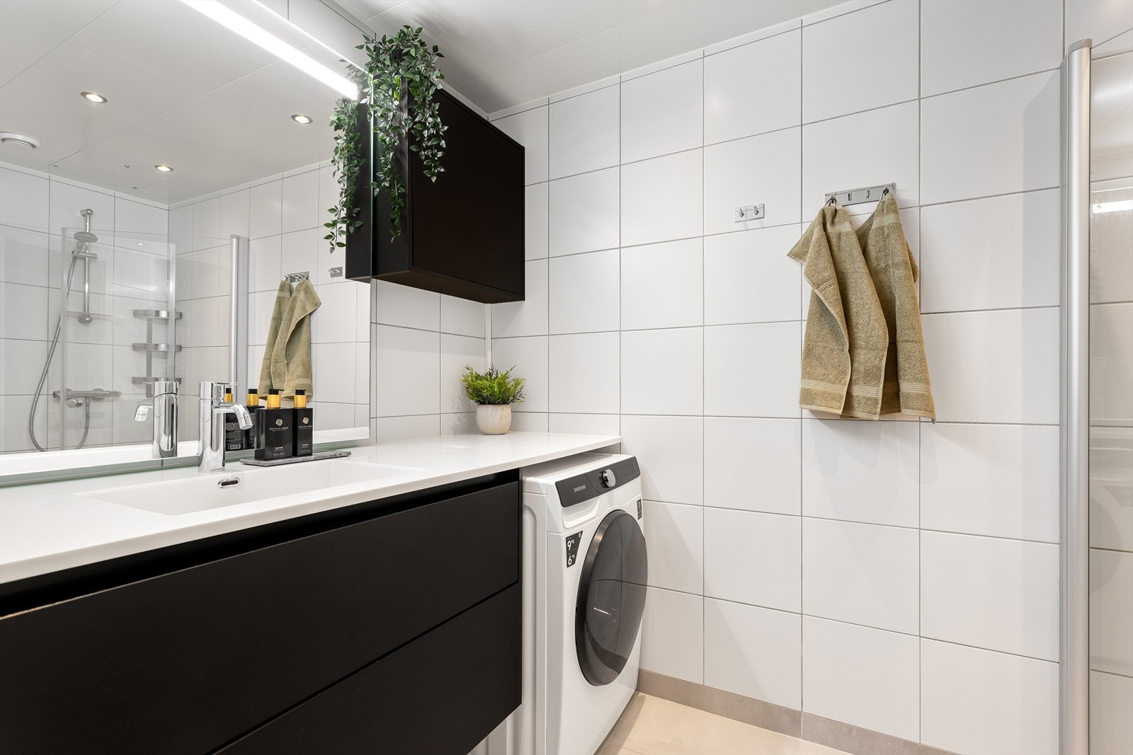 Lekkert og flislagt baderom med delikat og mørk innredning samt speil med lys. Galleribilde