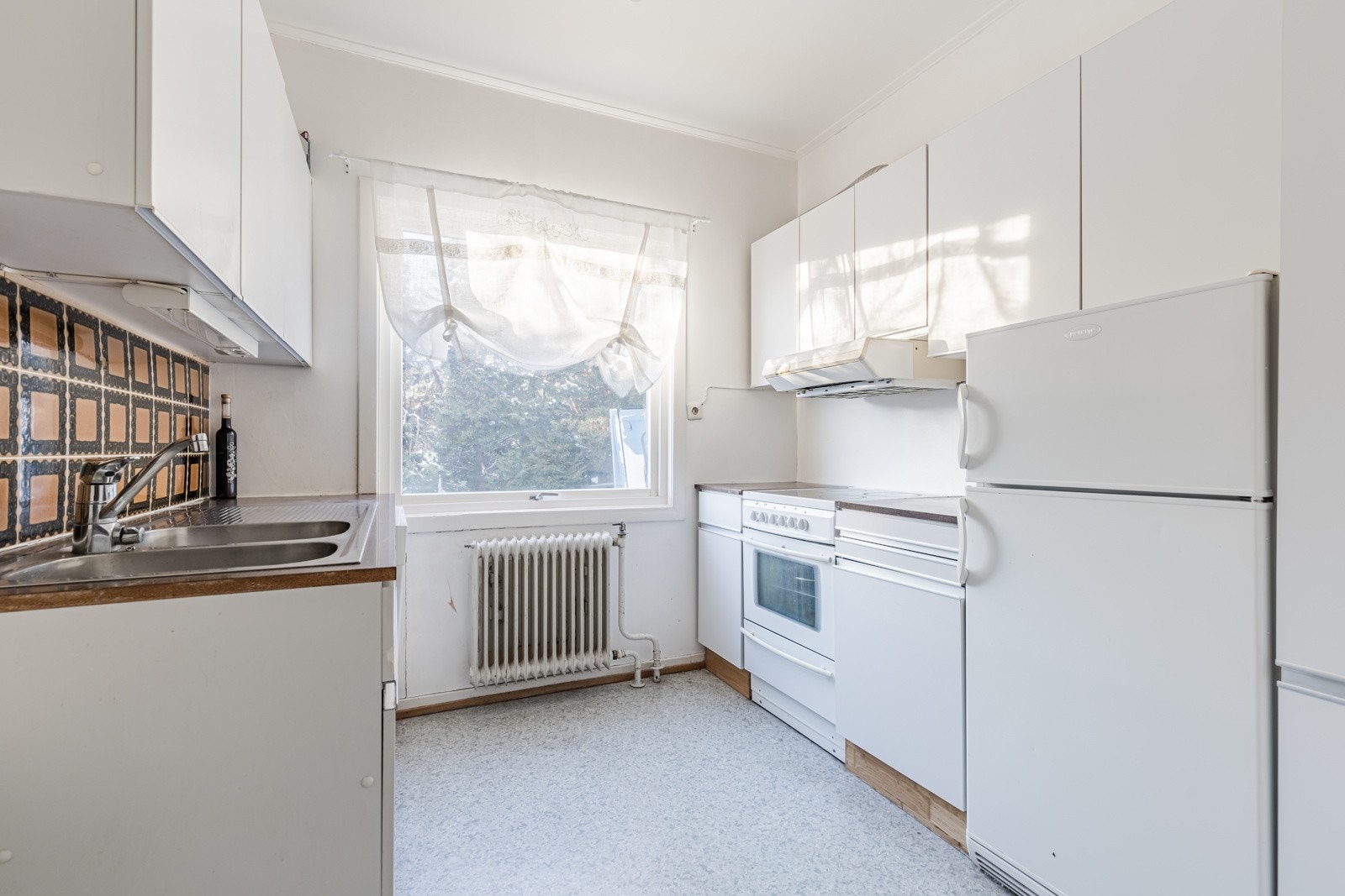 jøkkenet har gulvbelegg og hvitmalte vegger. Innredningen er oppført langs to vegger, med hvite, glatte fronter, dobbel oppvaskkum og laminert benkeplate. Av hvitevarer har kjøkkenet komfyr, oppvaskmaskin og en kombinert kjøl/frys. Galleribilde