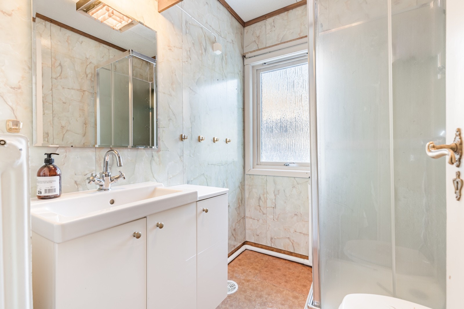 Badet har vinylbelegg på gulvet og mønstrede våtromsplater på veggene. På badet er det toalett og dusjkabinett. Baderomsinnredningen består av servant med hvite underskap og et speil med belysning. Det er opplegg for vaskemaskin. På soverommet står det e Galleribilde