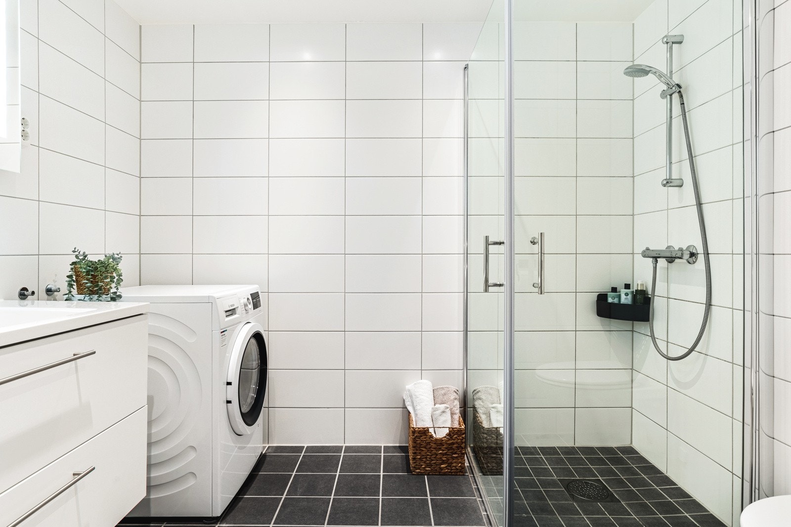 Flott helfliset baderom med vegghengt toalett, helstøpt servant, skuffer under servant og dusjdører i klart glass. Galleribilde