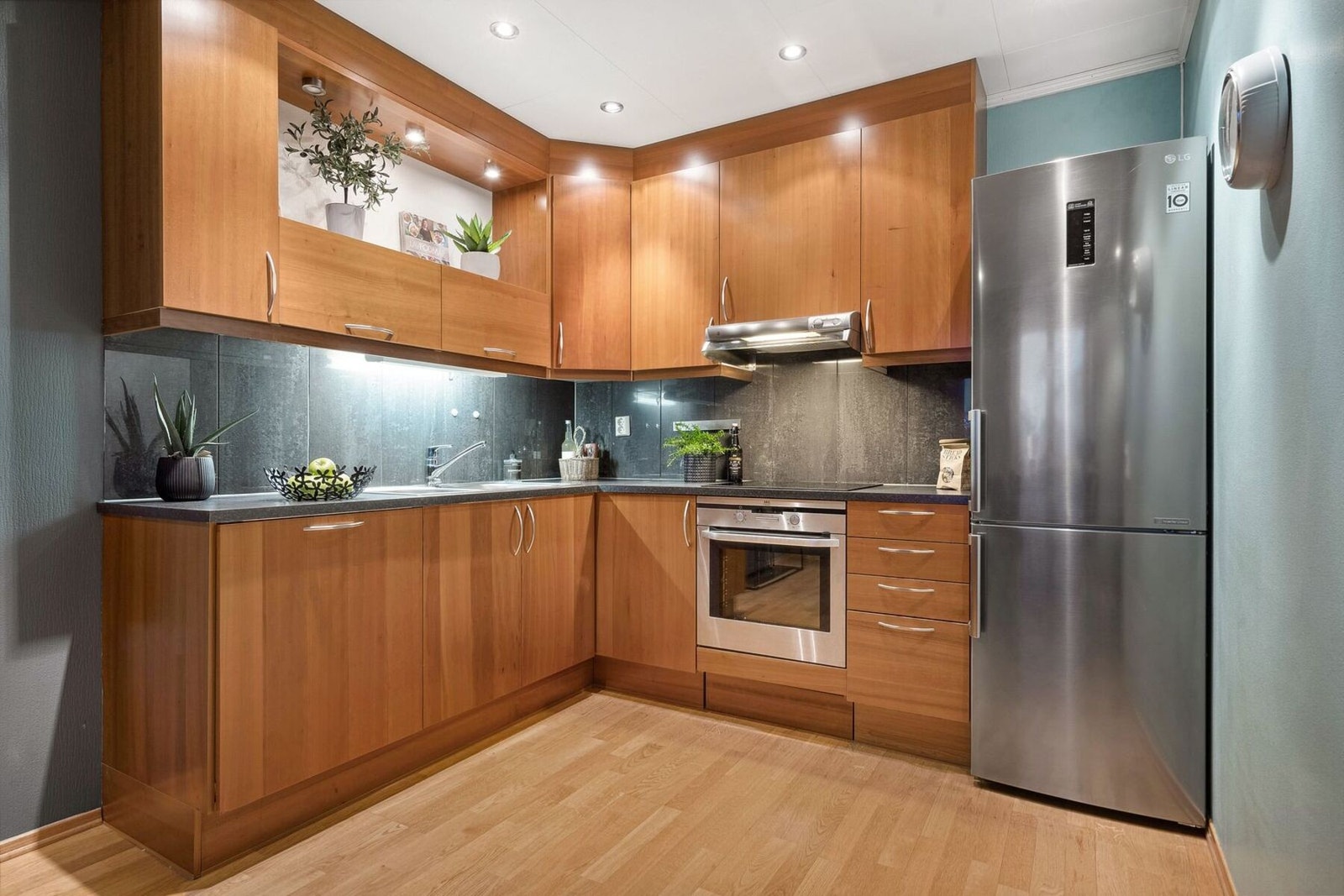 Innredning med slette trefargede fronter, benkeplate av laminat og mørke kitchenboard-plater på vegg over benk. Lysarmatur under overskap. Galleribilde