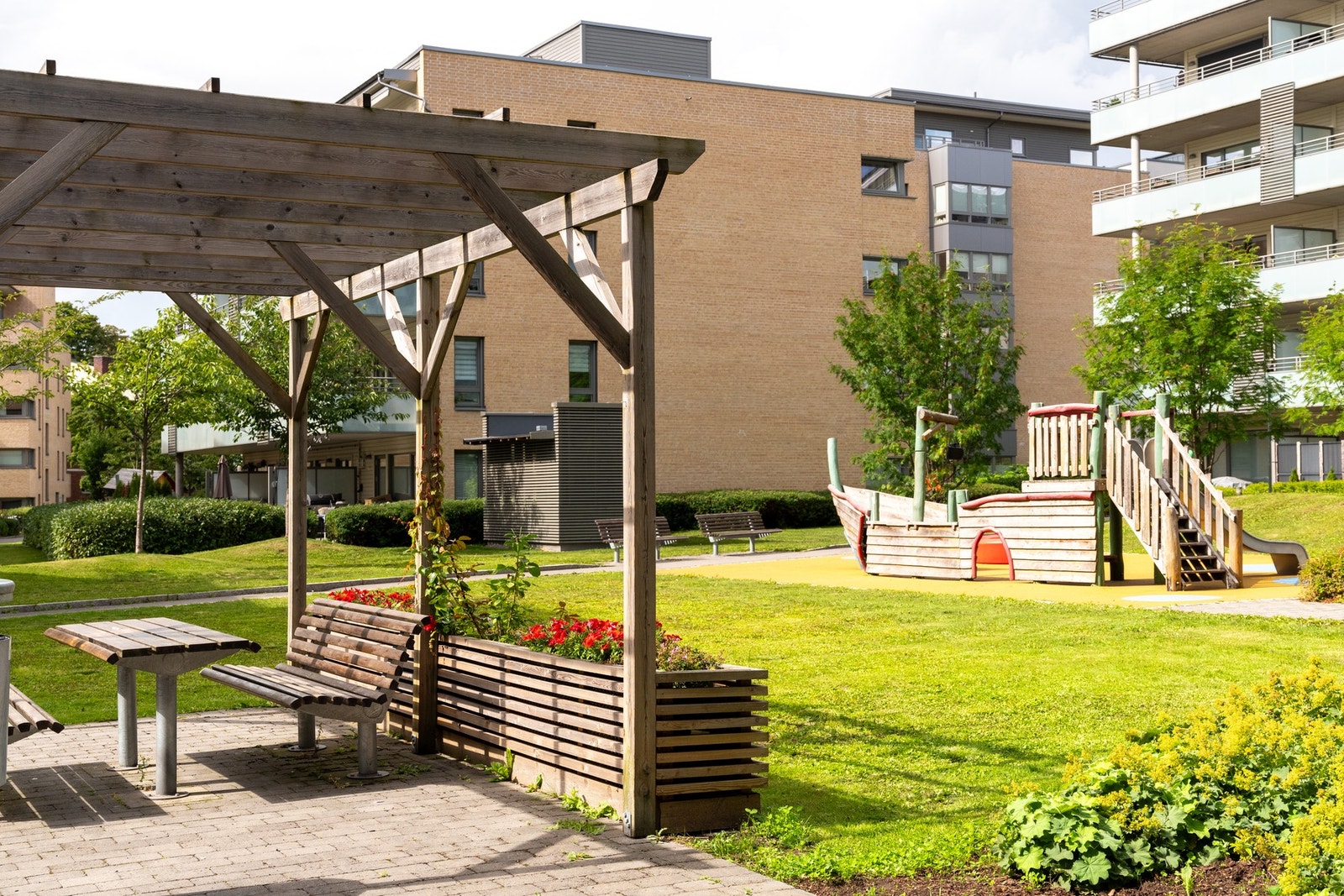 Boligens uteområde med fine grøntområder med pergola og sittebenker. Galleribilde