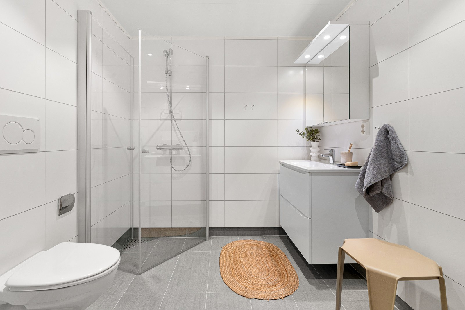 Bad med varmekabler i gulv, praktisk baderomsinnredning og dusj med innfellbare dører.
