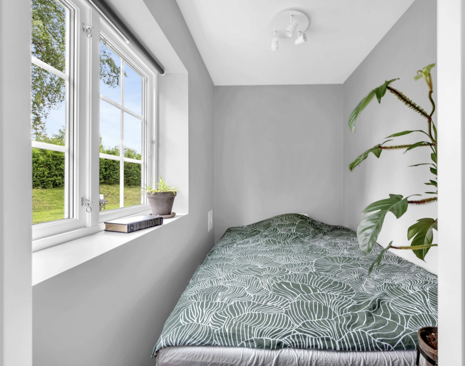 A small bedroom painted in a grey colour, with windows and room for a 120 cm bed (the bed on the picture is included). The bedroom has a practical window frame that can be used as a shelf. Galleribilde