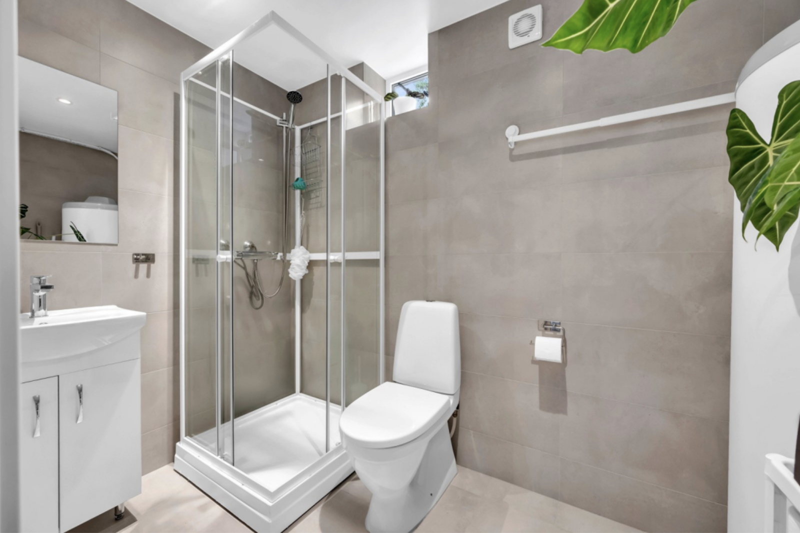 The bathroom has a modern feel to it and is equipped with a shower cubicle, washbasin furniture with matching base cabinet, a mirror above, as well as a toilet. Galleribilde