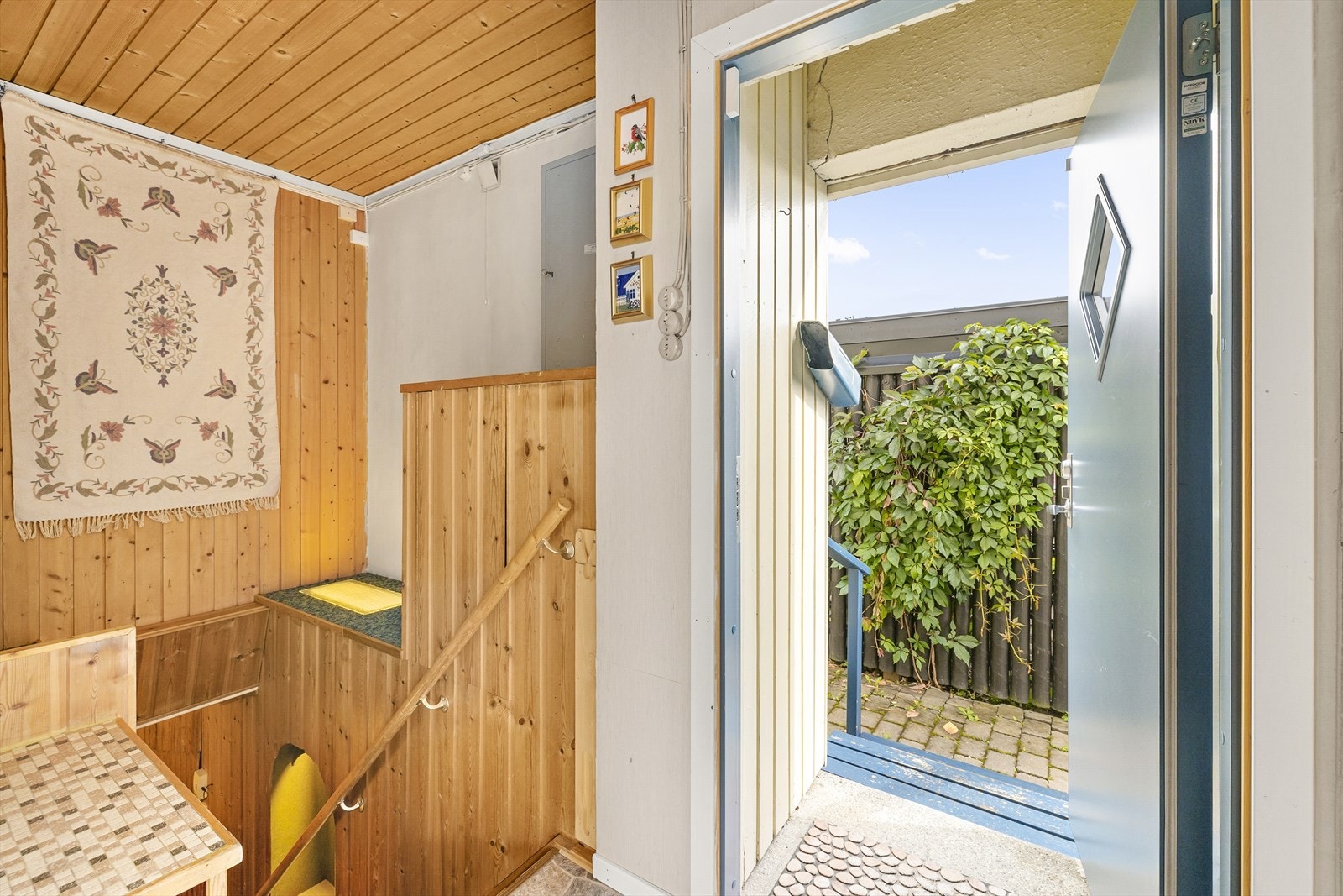 Entré med belegg på gulv, tekstilstrier på vegger og panel i tak. Trapp ned til underetasjen. Galleribilde