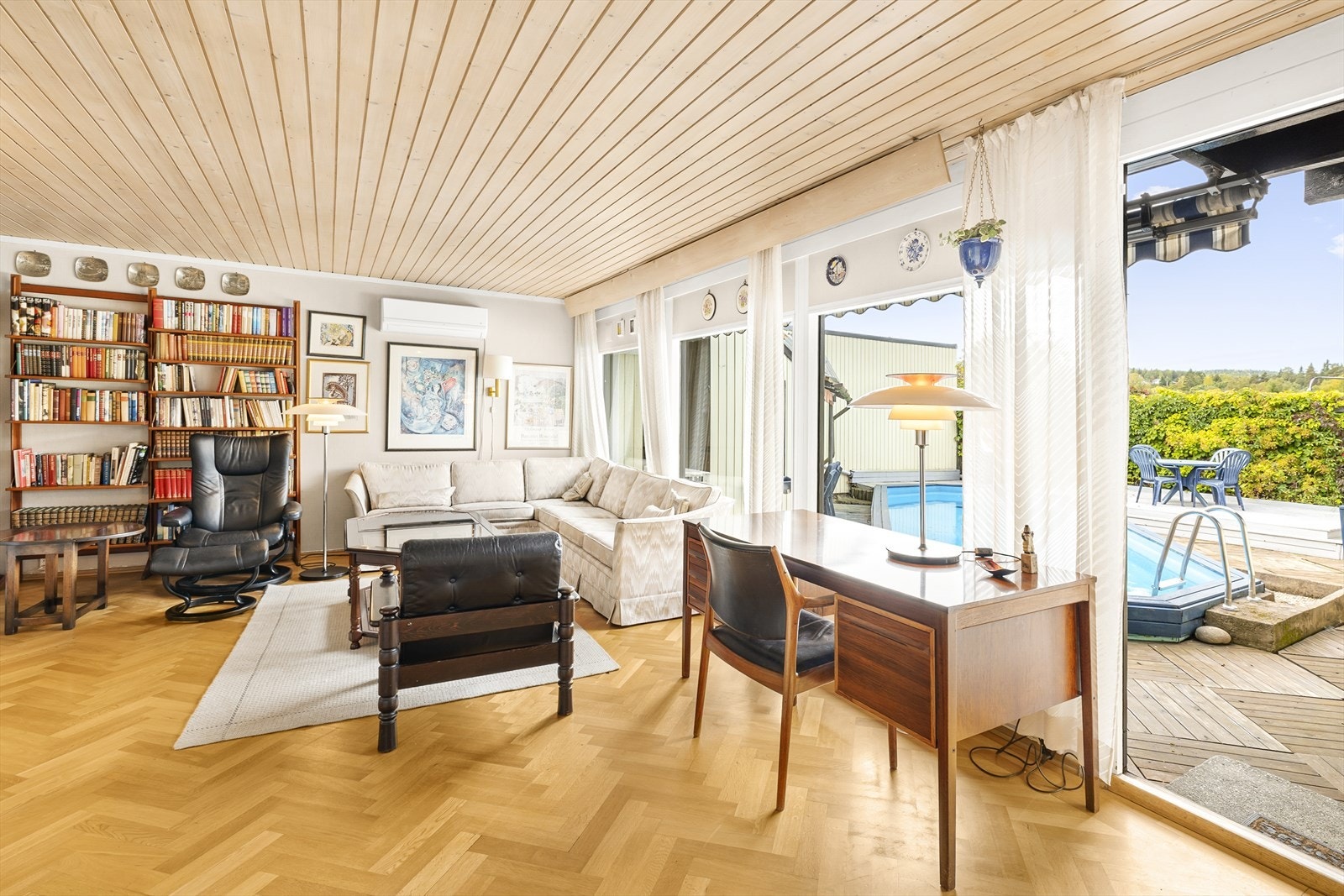 Romslig og luftig stue med parkett på gulv, strier på vegger og panel i tak. Det er montert peis med innsats og varmepumpe i stuen. Galleribilde