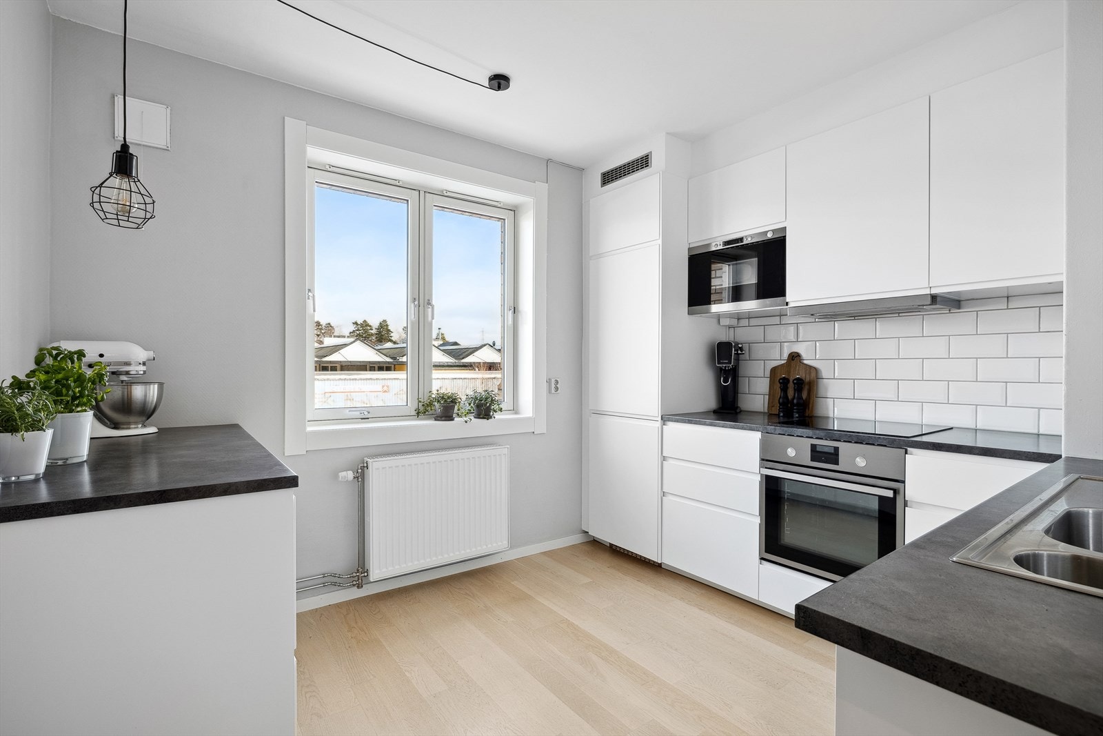 Pent IKEA kjøkken fra 2015 som har Innredning med glatte folierte fronter, laminat benkeplate med nedfelt kum i rustfritt stål, lys under overskap og fliser på vegg over benkeplaten. Galleribilde
