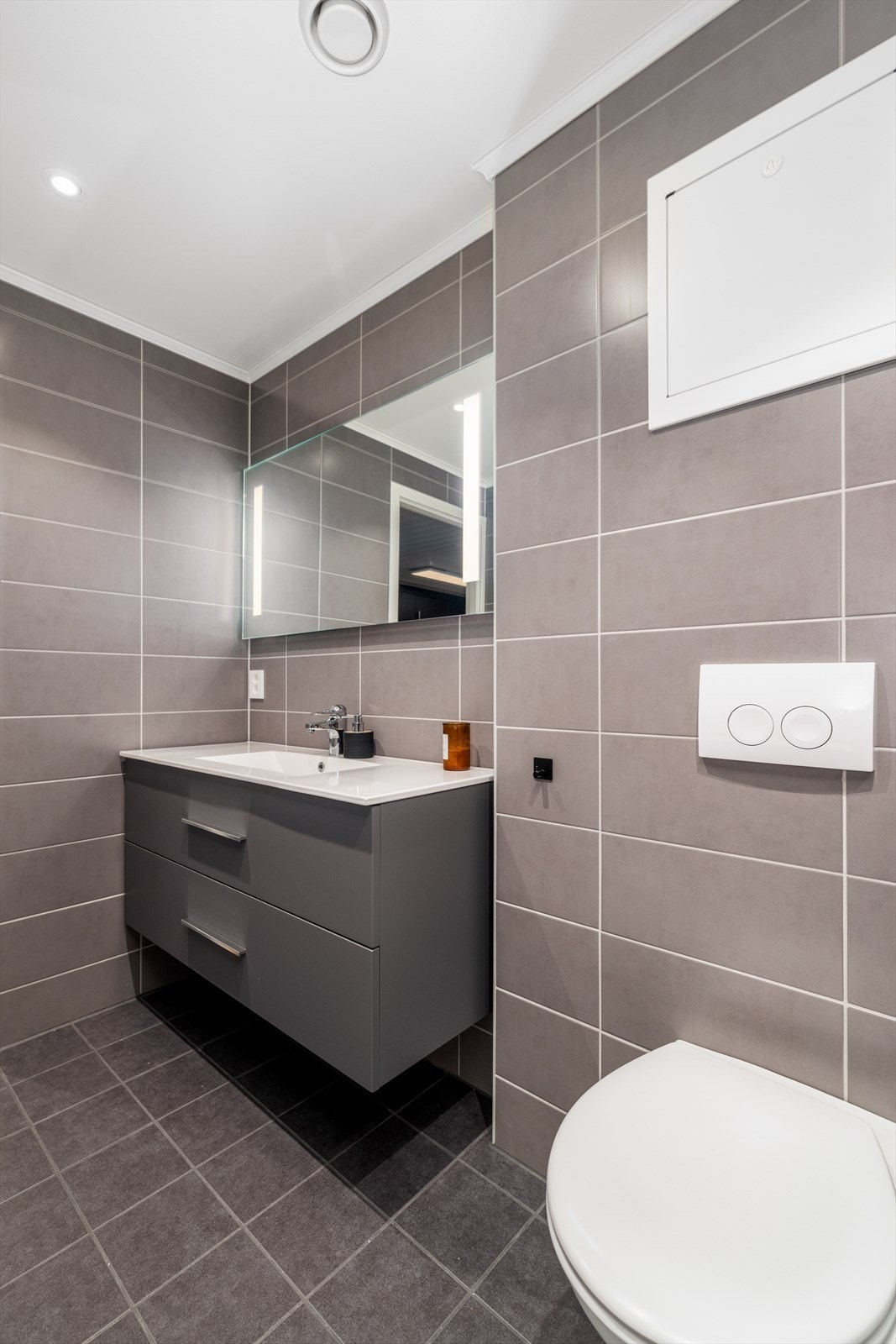 Den romslige innredningen på badet har dype skuffer for oppbevaring og heldekkende servant. Speil på vegg med integrert lys. Galleribilde