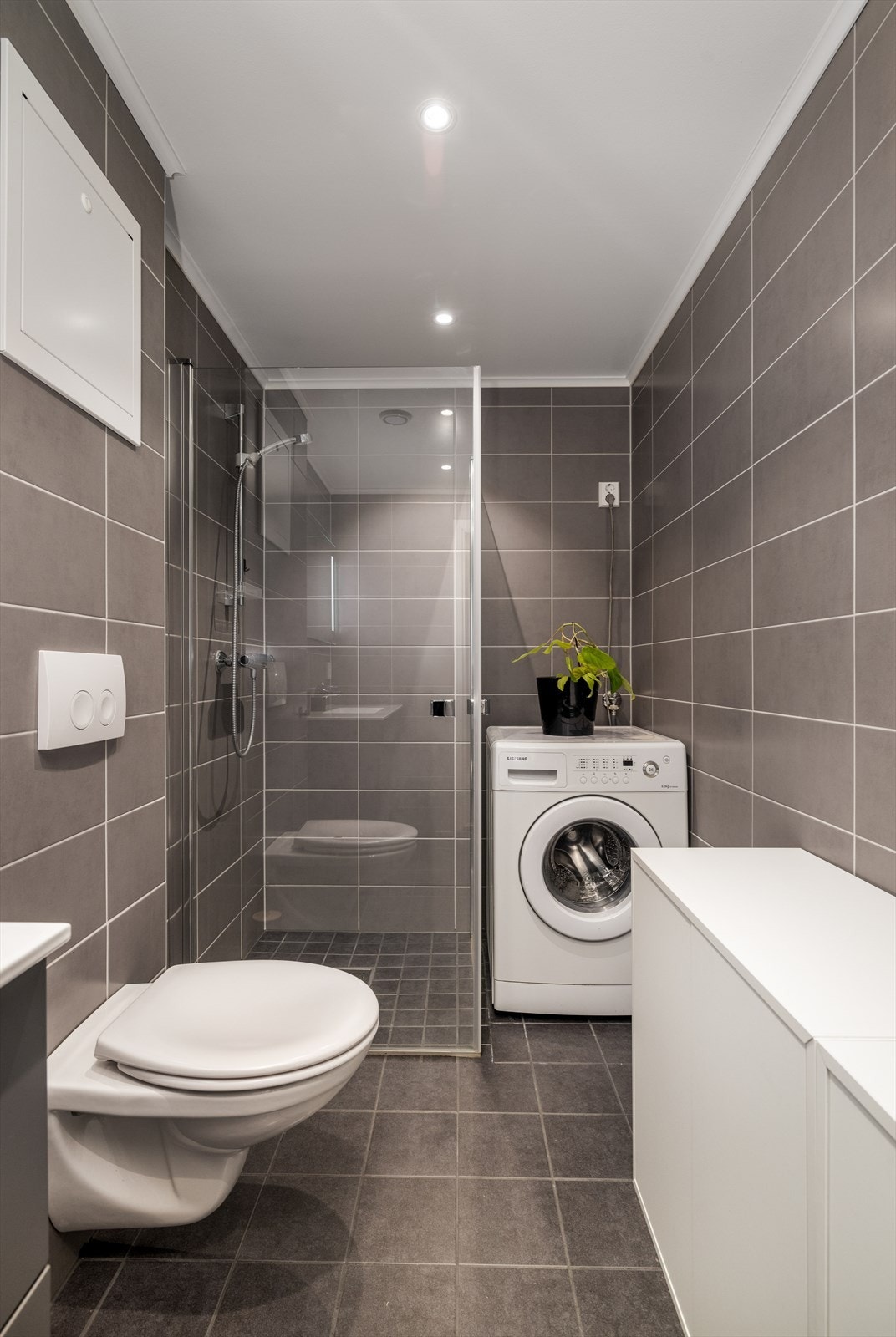 Badet har dusjhjørne med glassvegger samt veggmontert toalett. Her er også opplegg for og plass til vaskemaskin. Galleribilde