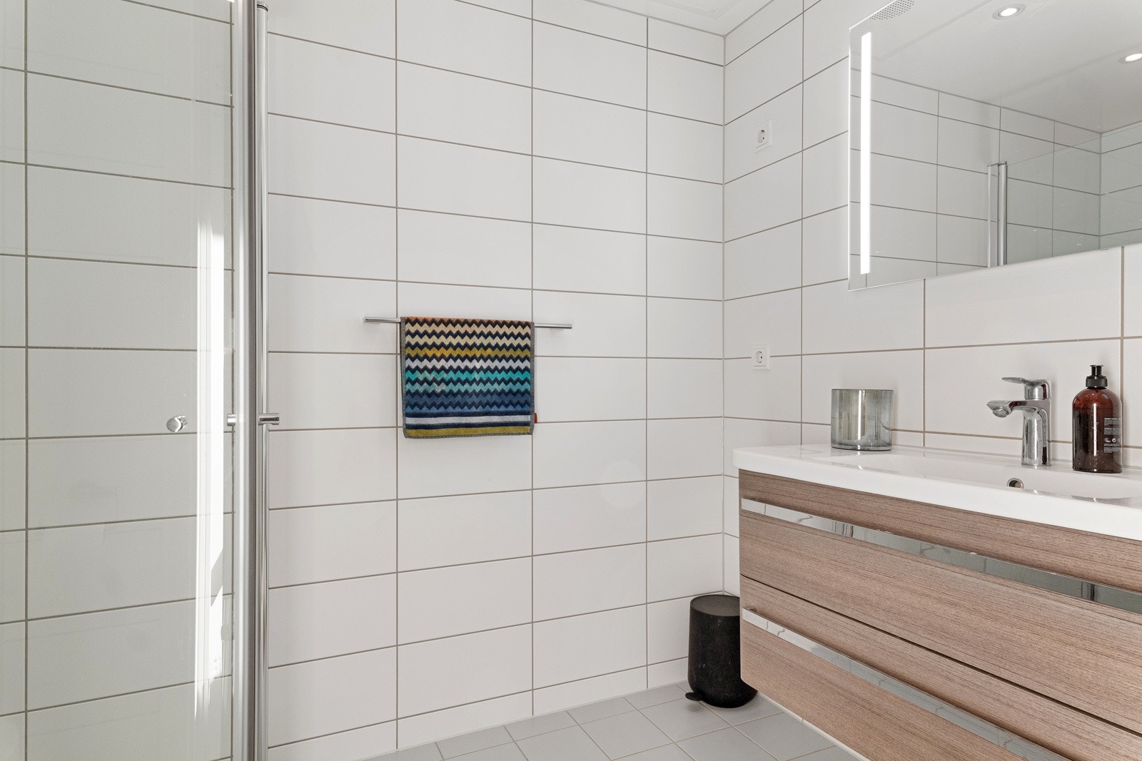 Badene er tilnærmet identiske, med lysegrå gulvfliser, hvite veggfliser, gulvvarme og downlights. Galleribilde