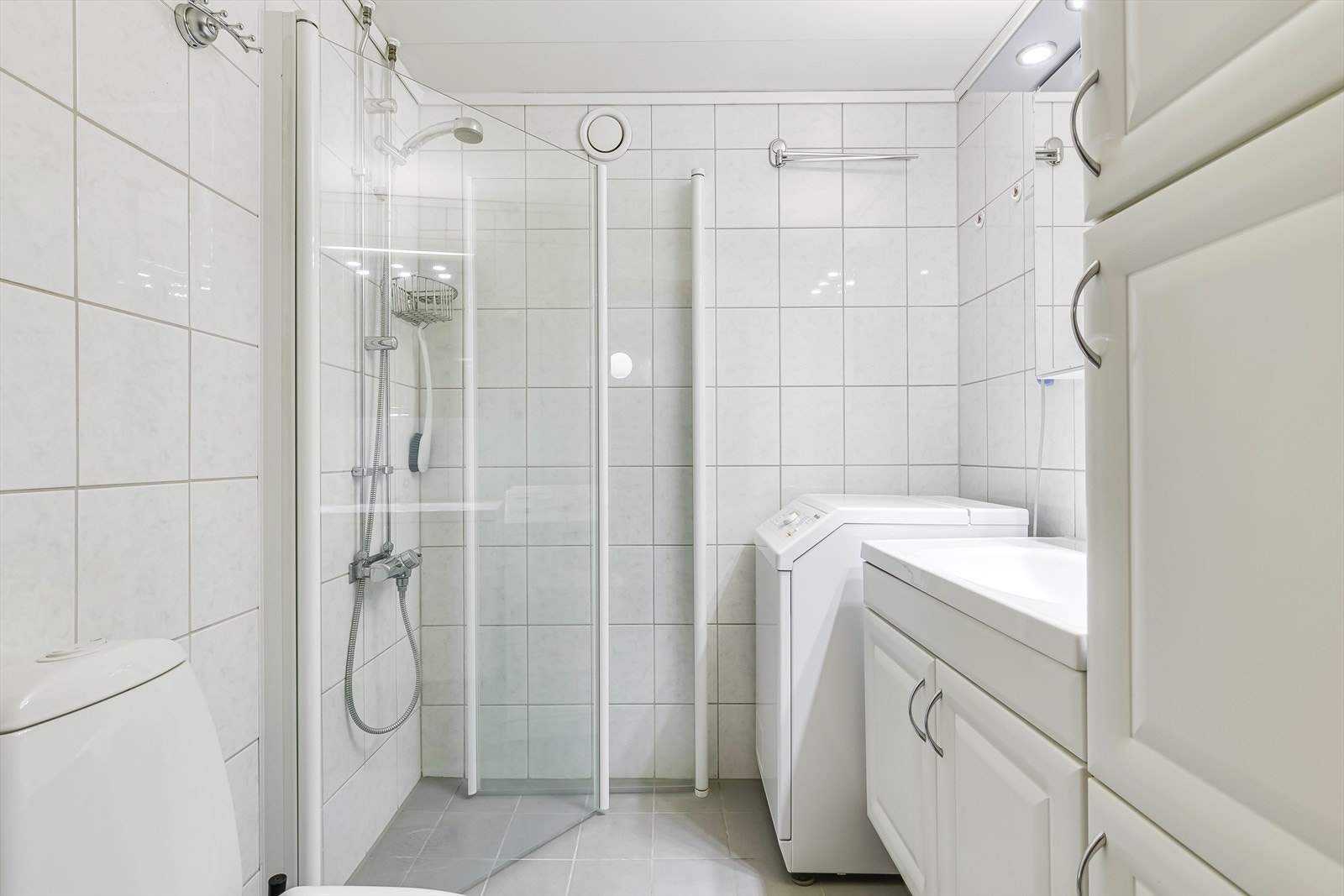 Badet er utstyrt med et gulvmontert toalett, en servantinnredning, et dusjhjørne med glassdører samt opplegg for vaskemaskin. Varmekabler i gulv. Galleribilde