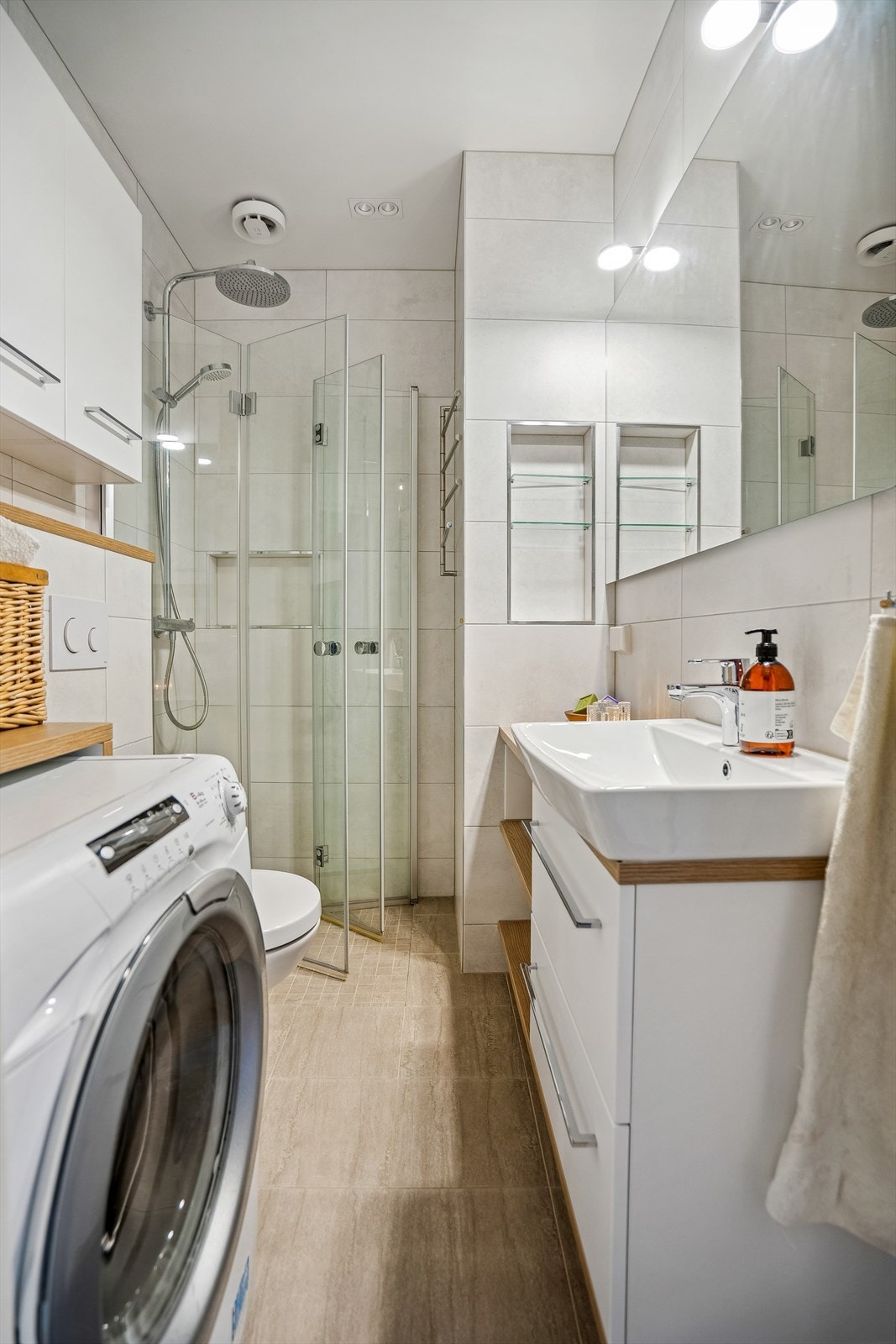 Badet er innredet med veggmonterte dusjvegger, veggmontert klosett, servant med skuffer, speil med belysning og opplegg for vaskemaskin. Galleribilde