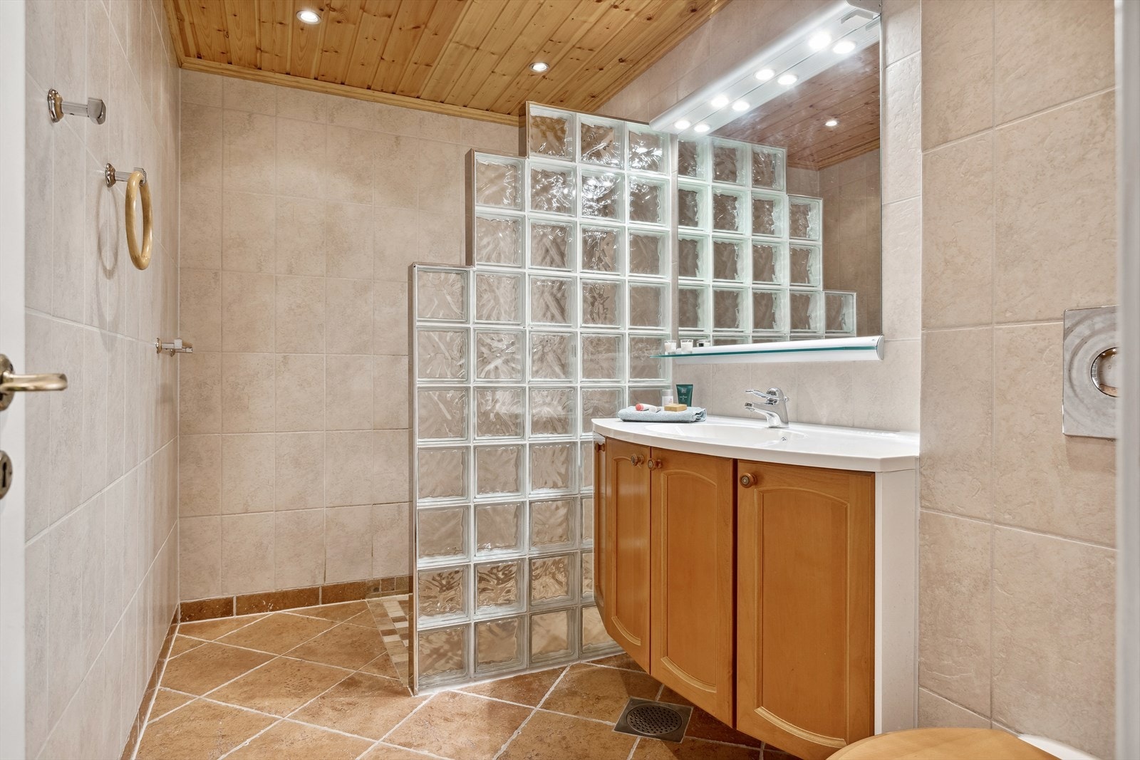 Badet er utstyrt med åpen dusj med oppmurt dusjvegg av glassbyggerstein, innredning med helstøpt servant, samt toalett med skjult sisterne. Galleribilde