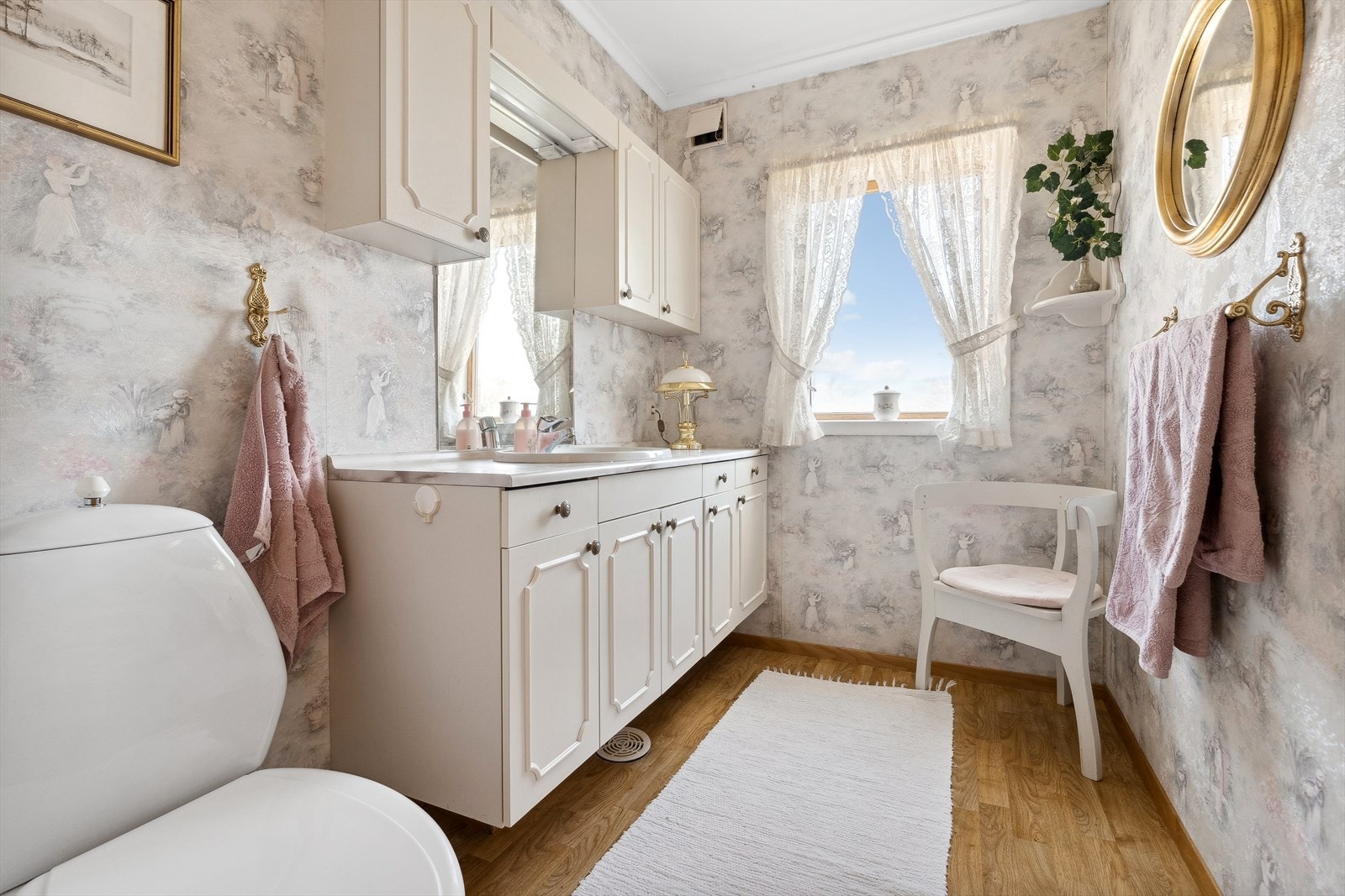 Toalettrom med belegg på gulv, tapet på vegger og seksjon med servant og toalett. Galleribilde