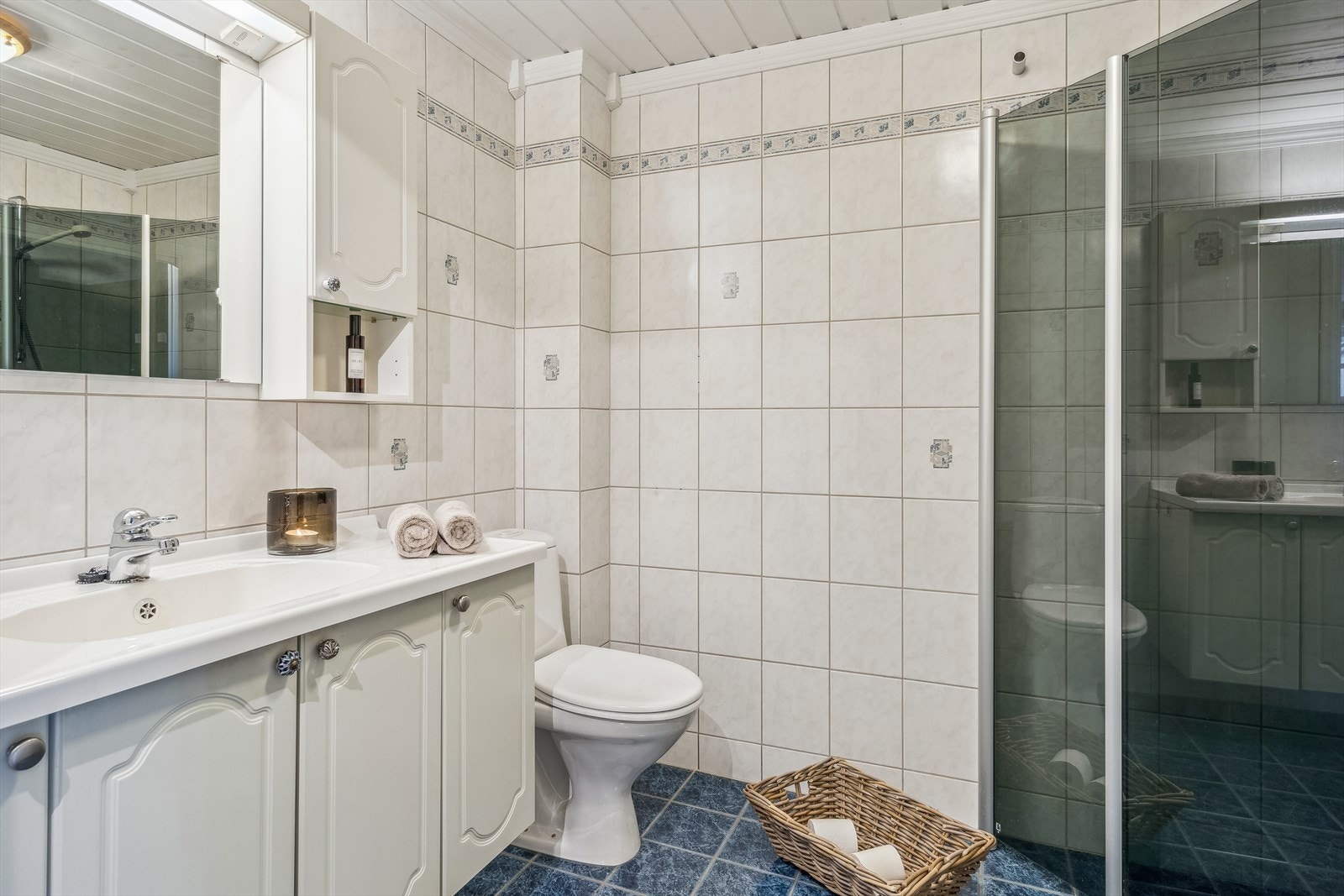 Bad fra byggeår belagt med fliser. Skapinnredning med servant, wc og dusjdører i glass. Galleribilde