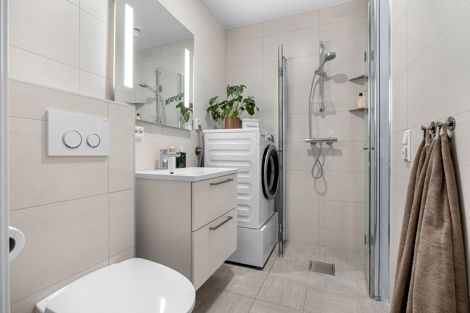 Badet er utstyrt med mekanisk avtrekk, innfellbare dusjdører, servantskap, opplegg for vaskemaskin og veggmontert wc. Galleribilde