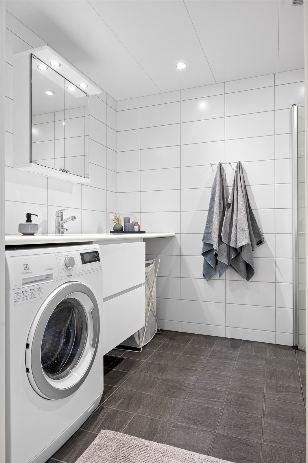 Badet har servant nedfelt i benkeplate som strekker seg fra vegg til vegg med opplegg for vaskemaskin og tørketrommel under benkeplaten Galleribilde