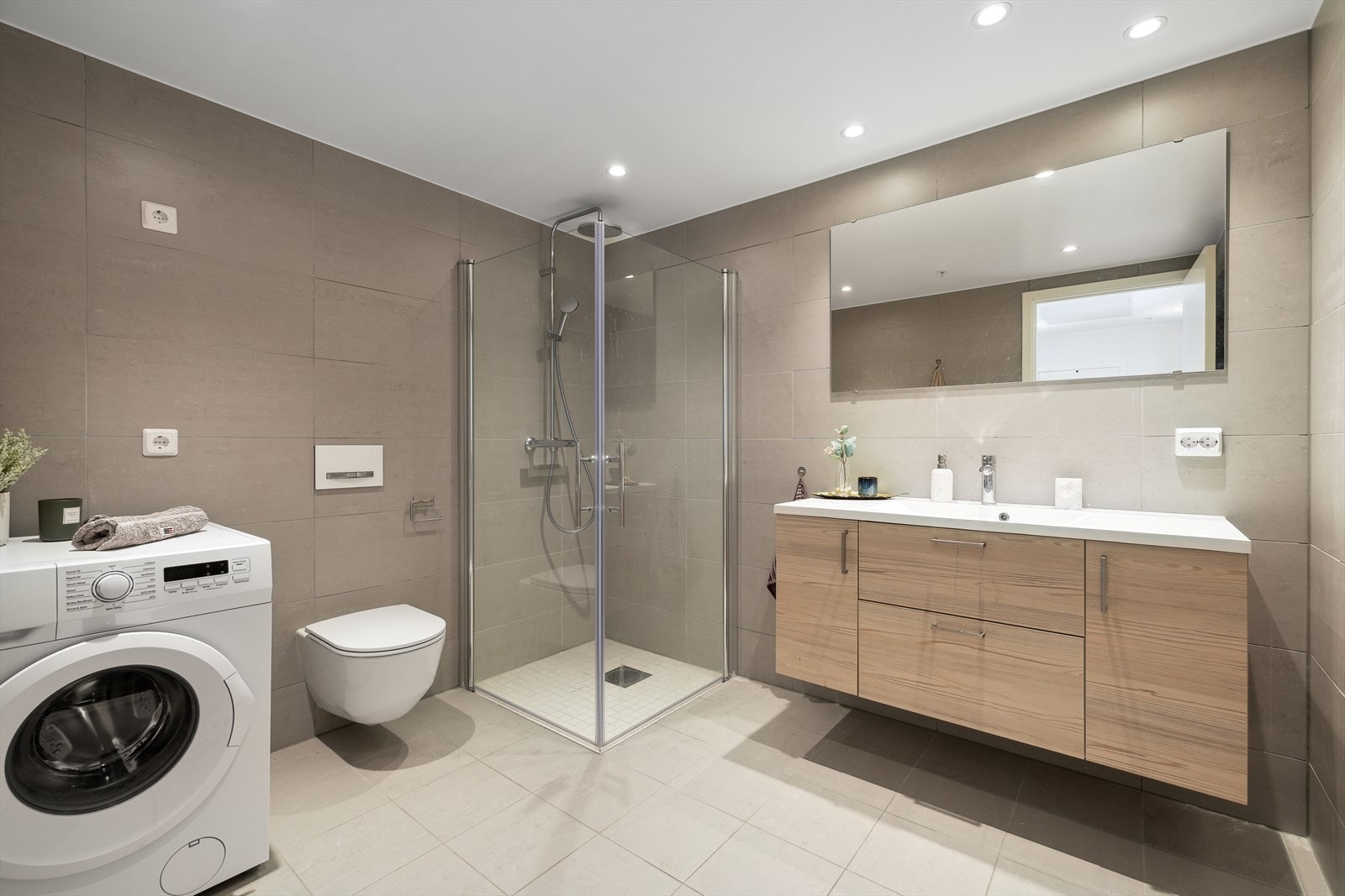 Baderomsinnedning med nedfelt servant, vegghengt toalett, dusjhjørne med innfellbare dører i herdet glass og speil. Galleribilde